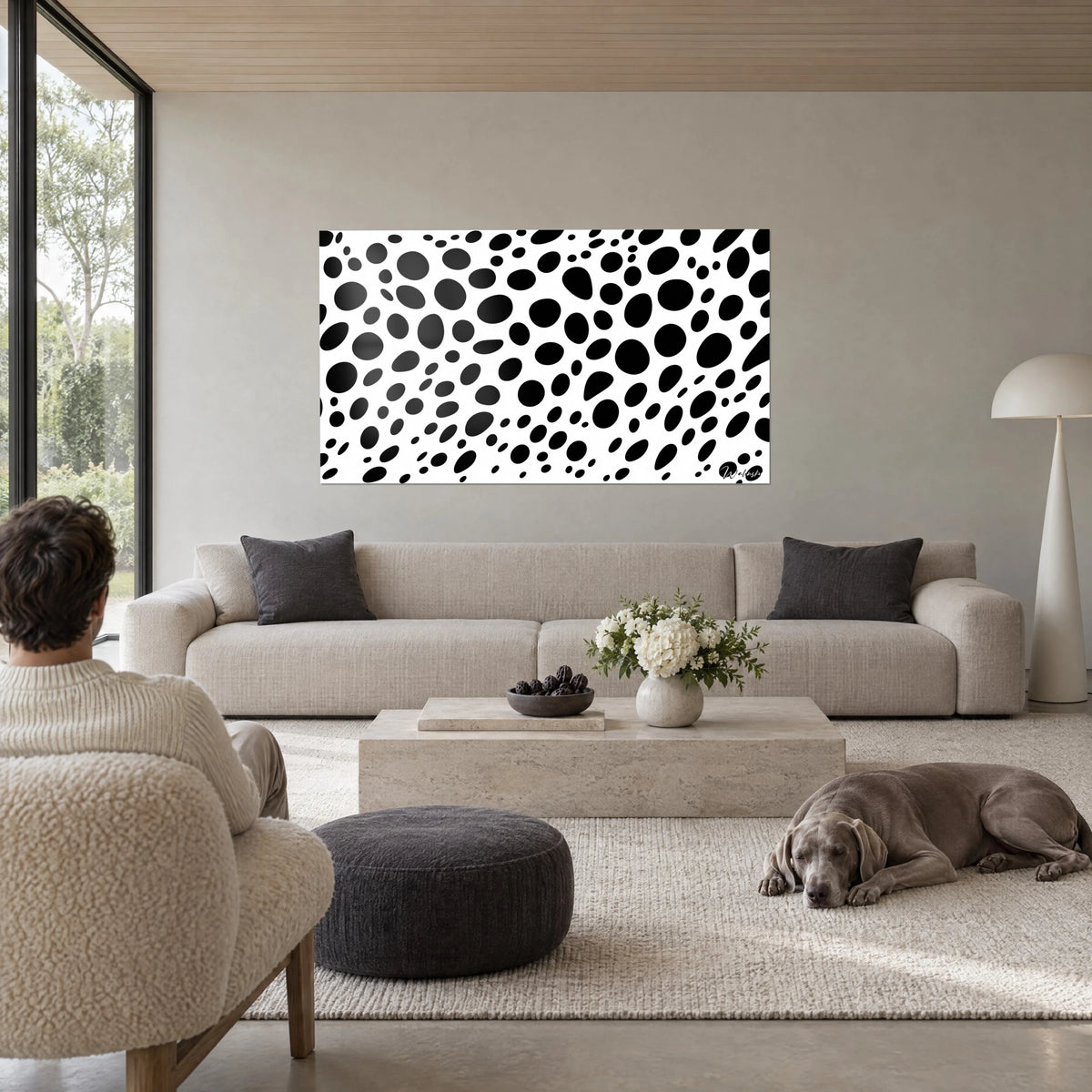 Tableau motif tacheté de grosses taches noires sur fond blanc, une personne de dos et un Weimaraner, au-dessus d'un canapé dans un salon lumineux
