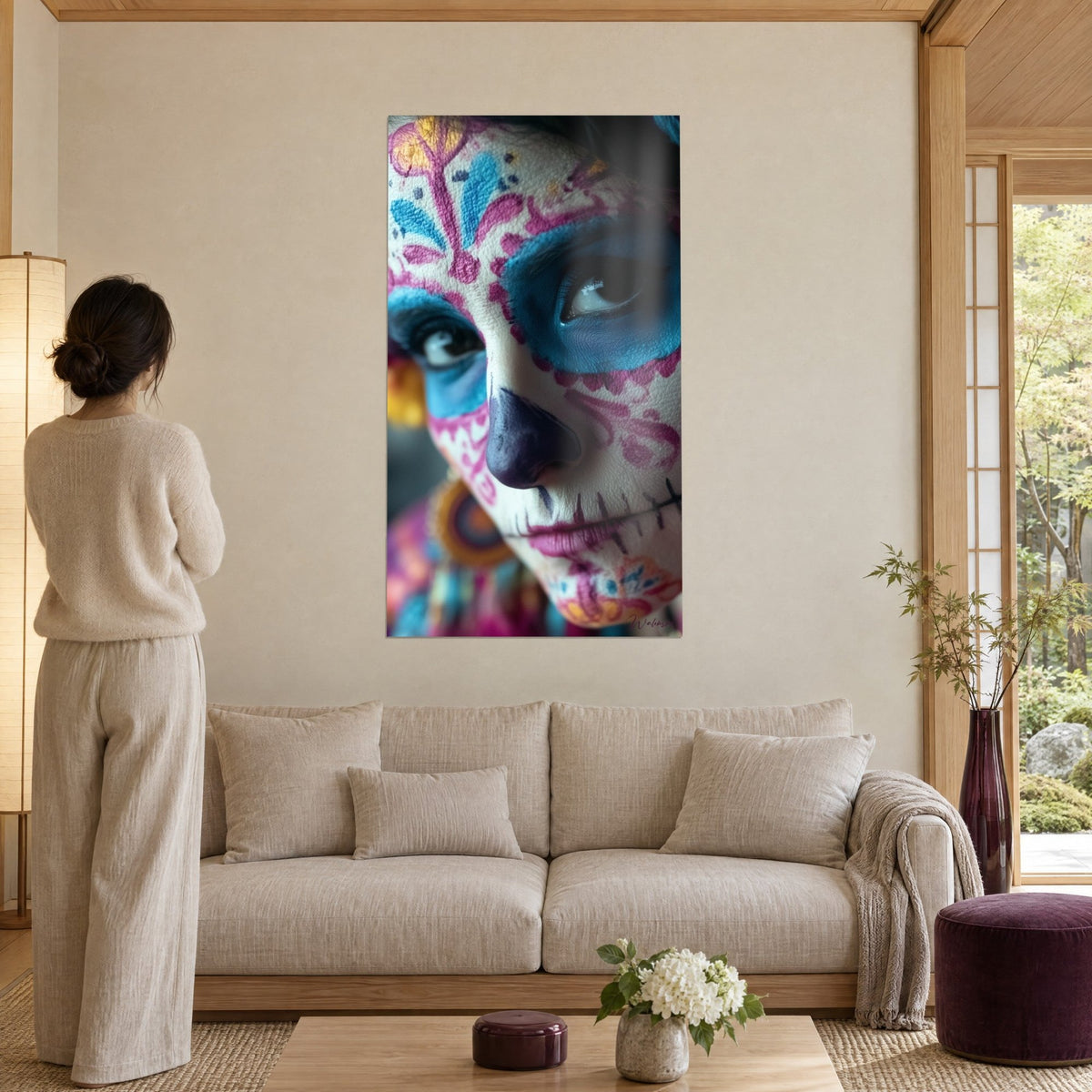 Quadro volto dipinto come calavera, naso viola e motivi rosa e blu, appeso in un soggiorno japandi sopra un divano in una stanza luminosa