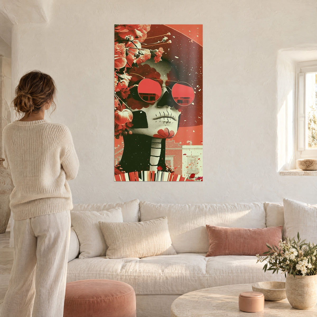 Gemälde Kalavera mit runden roten Brillen und korallenfarbenen Blüten, lachsfarbener Hintergrund, Frau von hinten über einem Sofa in einem hellen Wohnzimmer