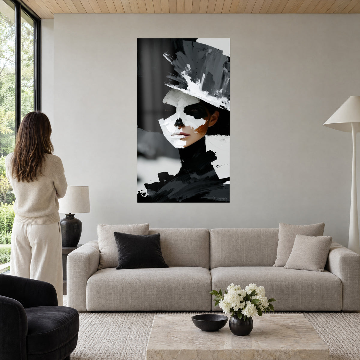 Tableau visage masqué à la peinture blanche épaisse, large chapeau gris et noir, femme de dos, au-dessus d'un canapé dans un salon lumineux