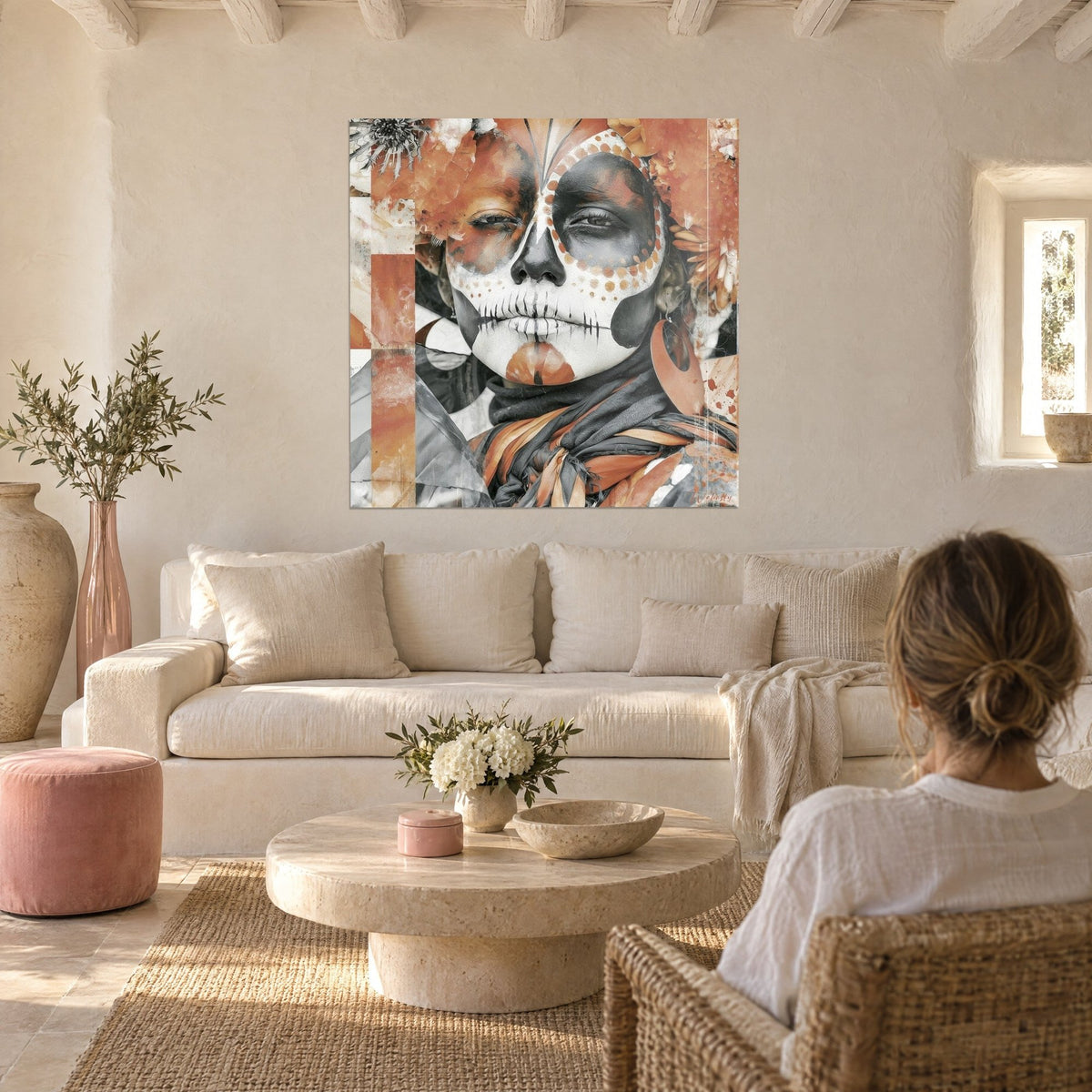 Cuadro rostro de calavera con pómulos punteados, en terracota y gris, de una mujer, sobre un sofá en un salón luminoso