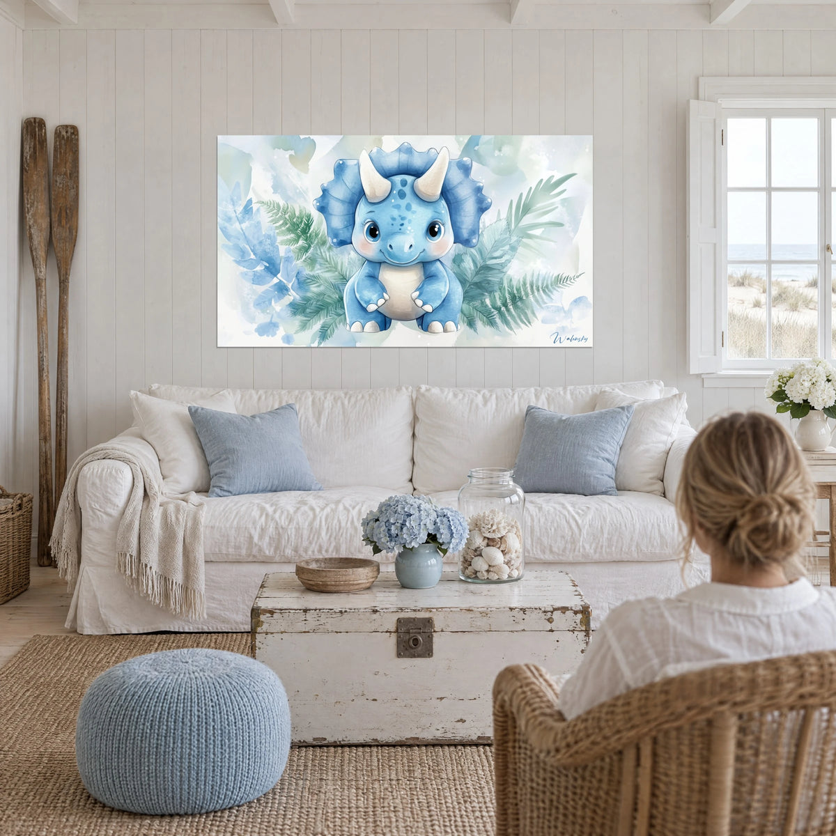 Wall art baby triceratops in blue with large black eyes, sage green fern fronds, above a sofa in a bright living room