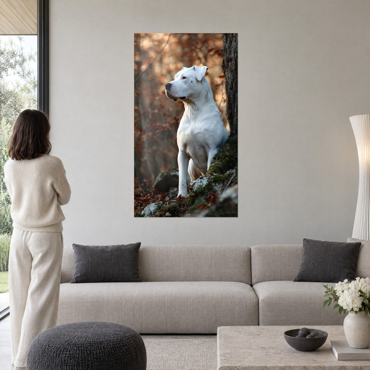 Tableau dogue argentin blanc assis contre un tronc moussu, feuillage cuivré, femme de dos, au-dessus d'un canapé dans un salon lumineux