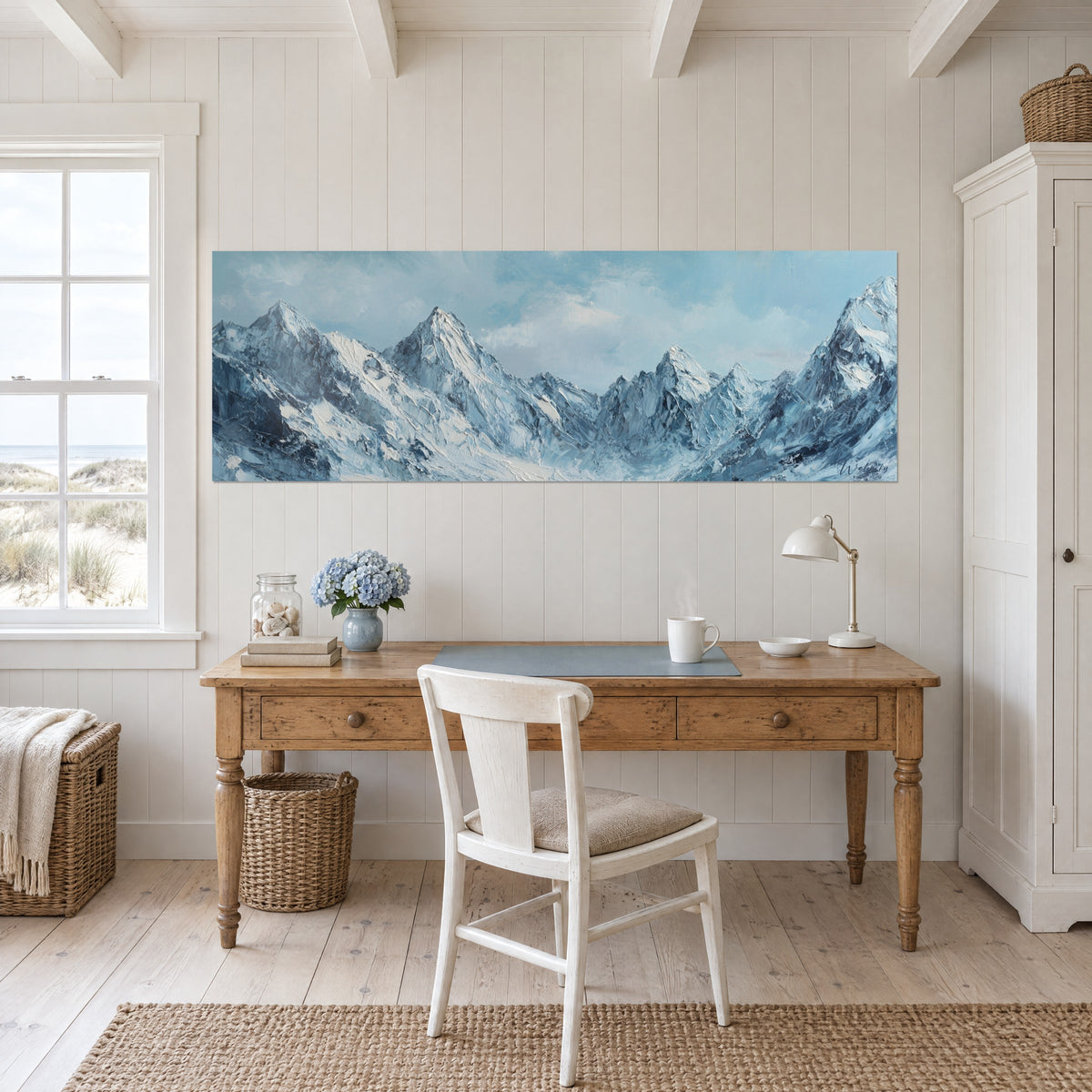 Cuadro paisaje de alta montaña helado, aristas azul denim y blanco nacarado, colgado encima de un escritorio de madera clara
