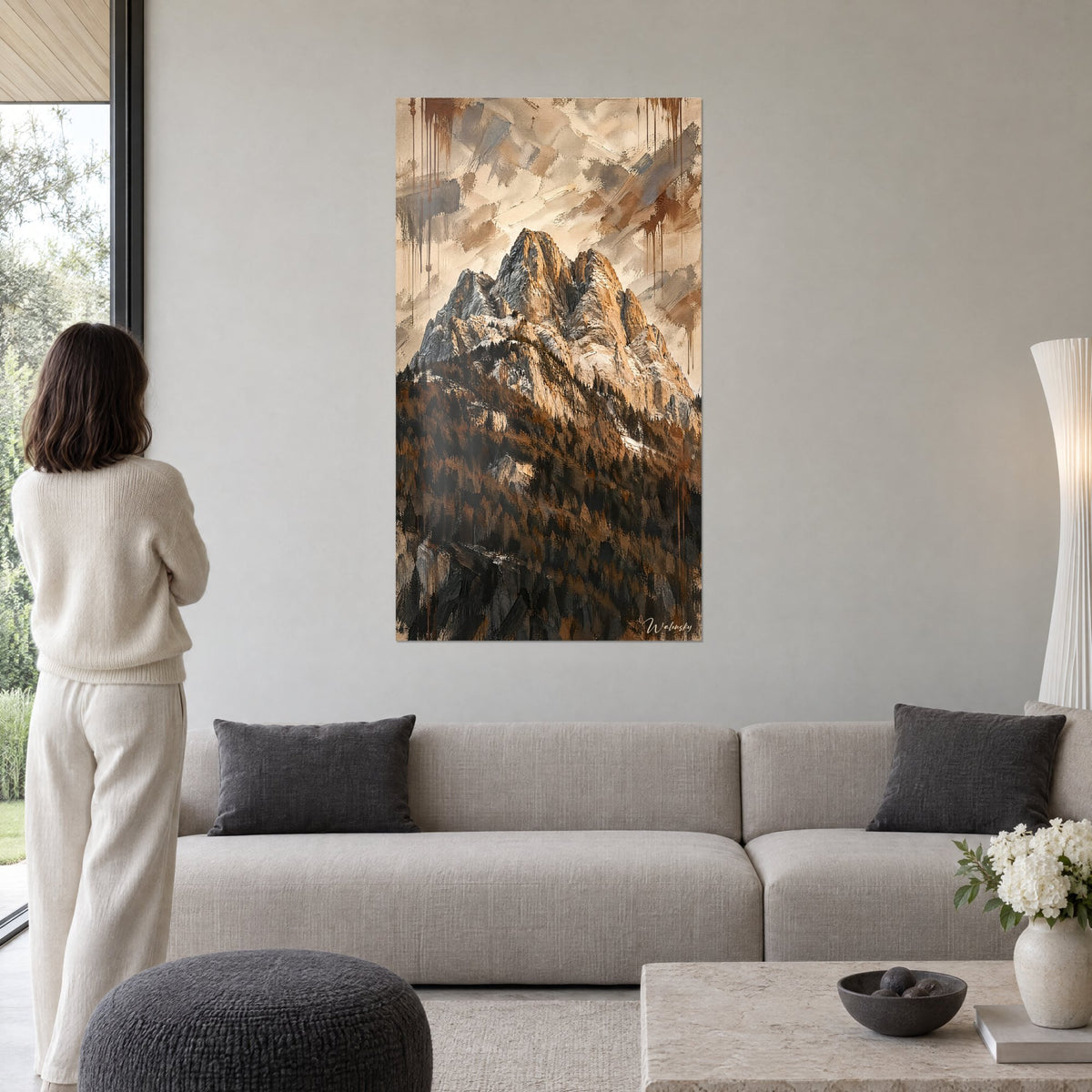 Tableau cime dolomitique ocre et gris, forêt sombre en bas, coulures brunes, femme de dos au-dessus d'un canapé dans un salon lumineux