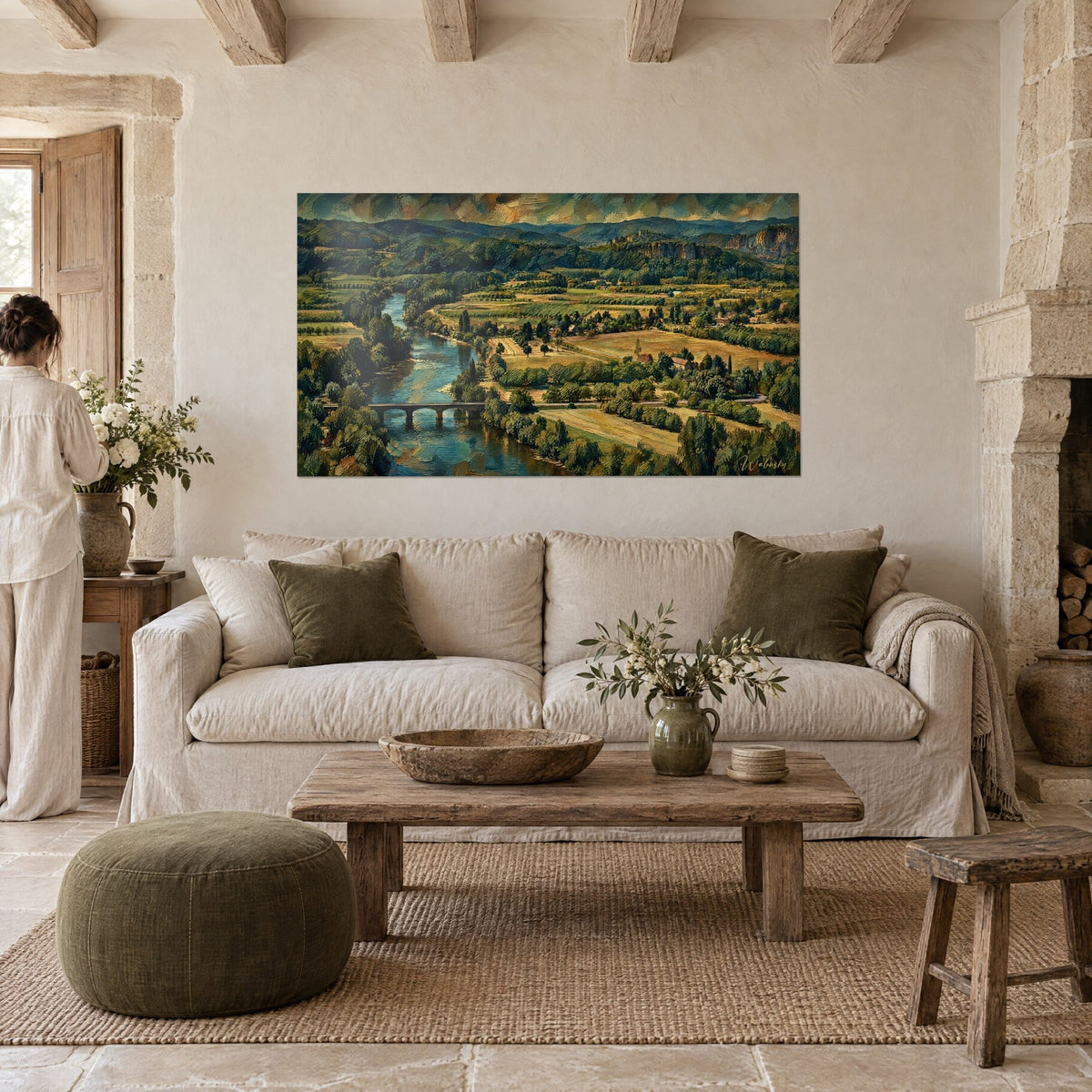 Wall art of a winding emerald-green river, stone bridge and golden fields, person seen from behind, above a sofa in a bright living room