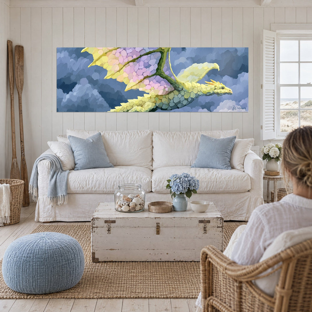 Tableau dragon jaune citron aux ailes lilas et rose volant parmi les nuages bleus, au-dessus d'un canapé dans un salon lumineux