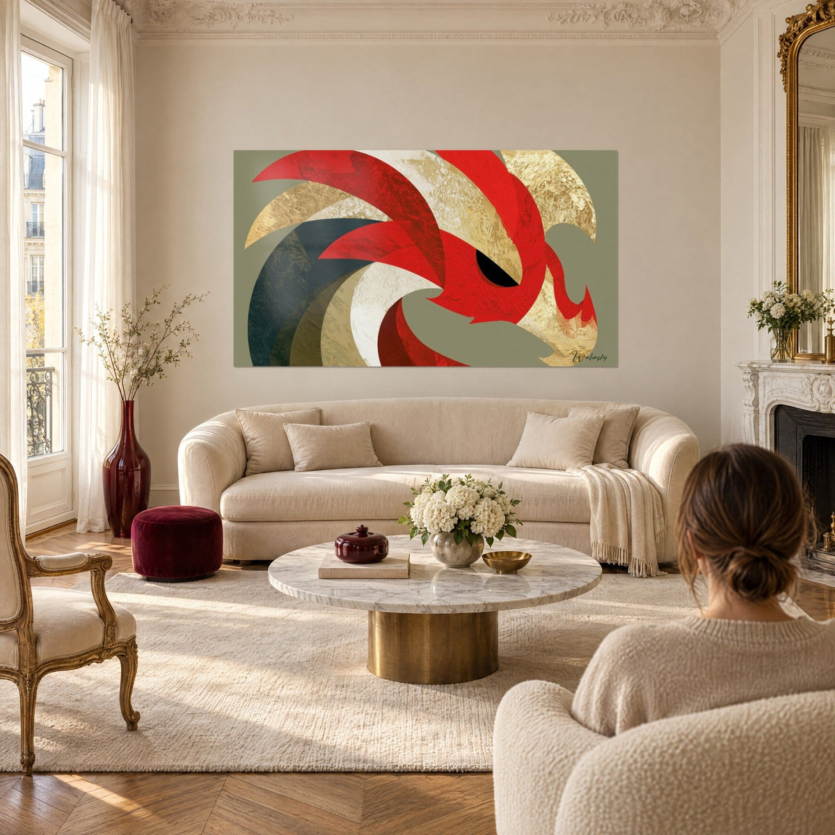 Tableau dragon stylisé aux plumes rouges et dorées, œil noir, fond vert sauge, femme de dos au-dessus d'un canapé dans un salon lumineux
