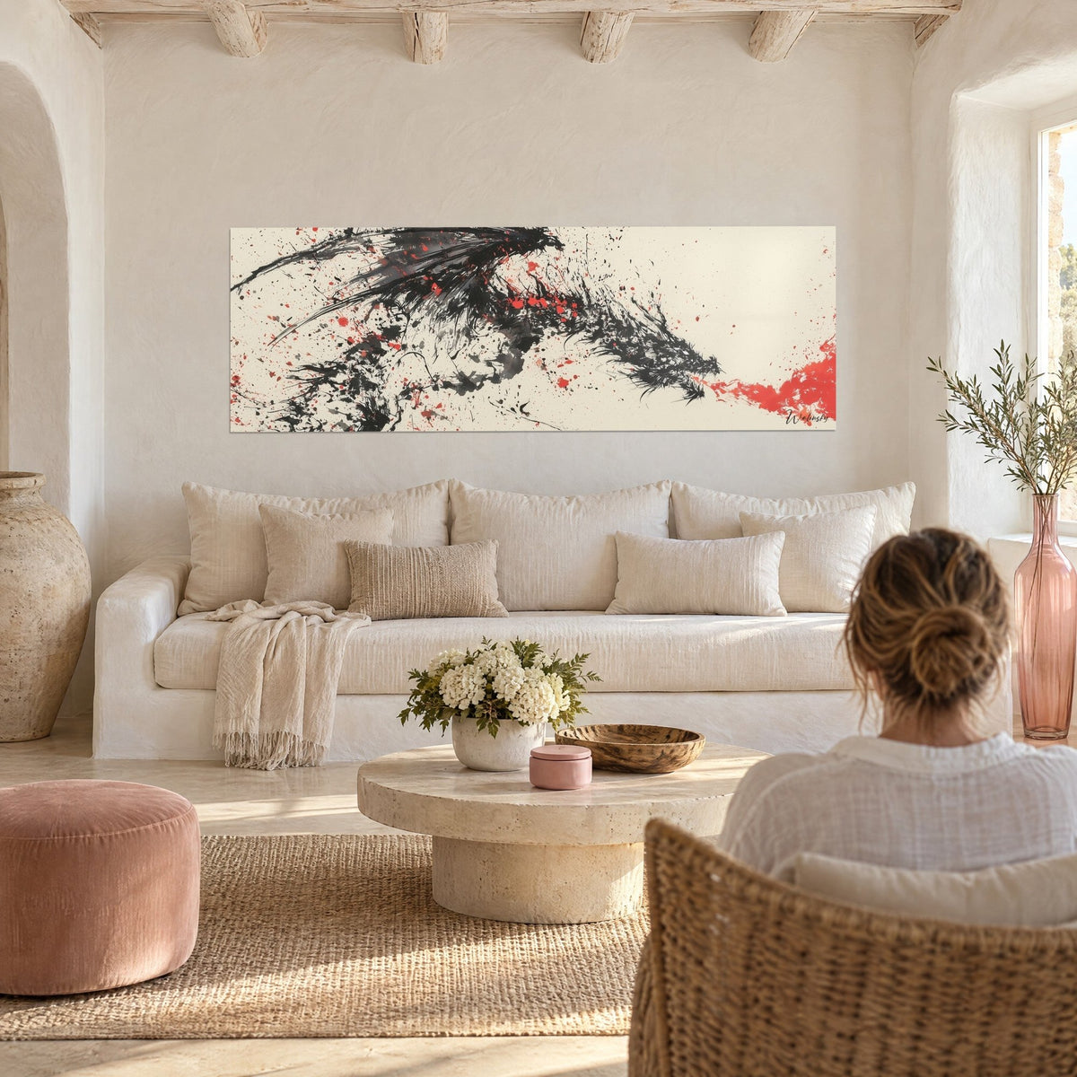 Cuadro dragón de tinta negra con alas desplegadas, salpicaduras rojas sobre fondo marfil, encima de un sofá en un salón luminoso