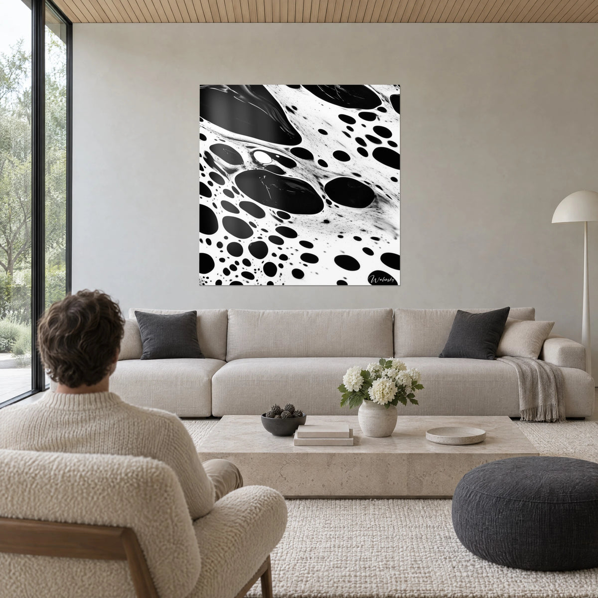 Quadro di pozzanghere di inchiostro nero a bolle su fondo bianco crema, uomo di spalle, sopra un divano in un soggiorno luminoso