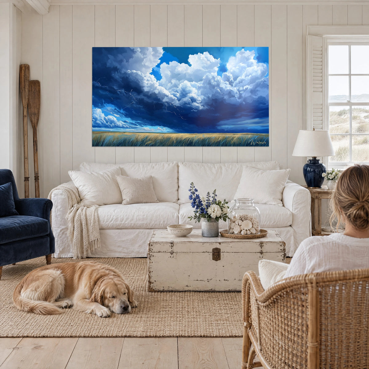 Cuadro de una tormenta amenazante sobre un campo de trigo, nubes azul medianoche y blancas, rayos finos, encima de un sofá en un salón luminoso