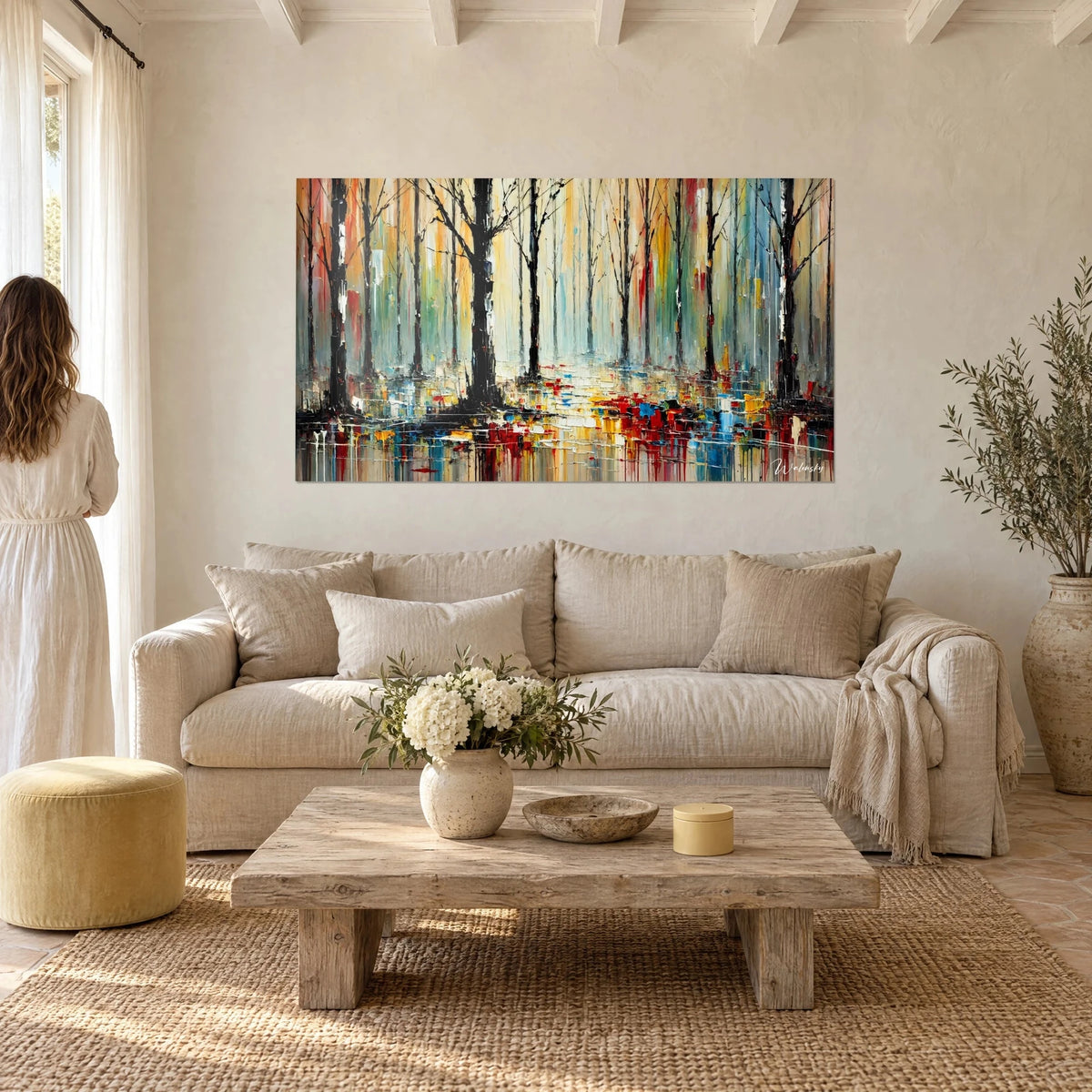 Wall art forest floor of black trees with red and blue drips, couple seen from behind, above a sofa in a bright living room