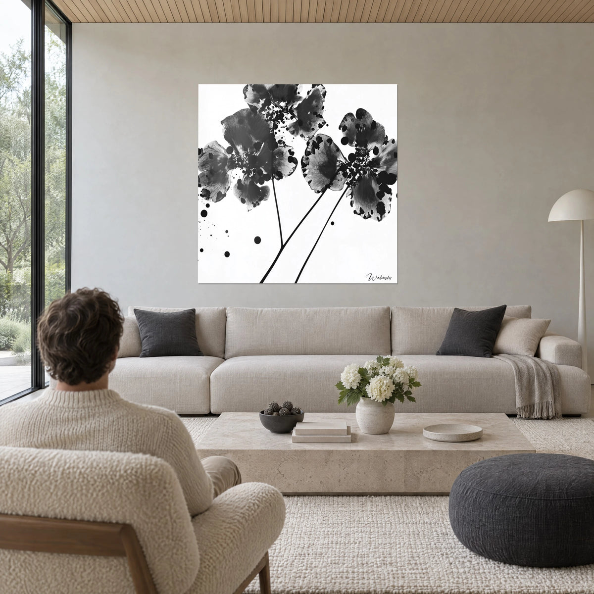 Cuadro de flores de tinta con pétalos veteados en negro y gris, salpicaduras sobre fondo blanco, encima de un sofá en un salón luminoso