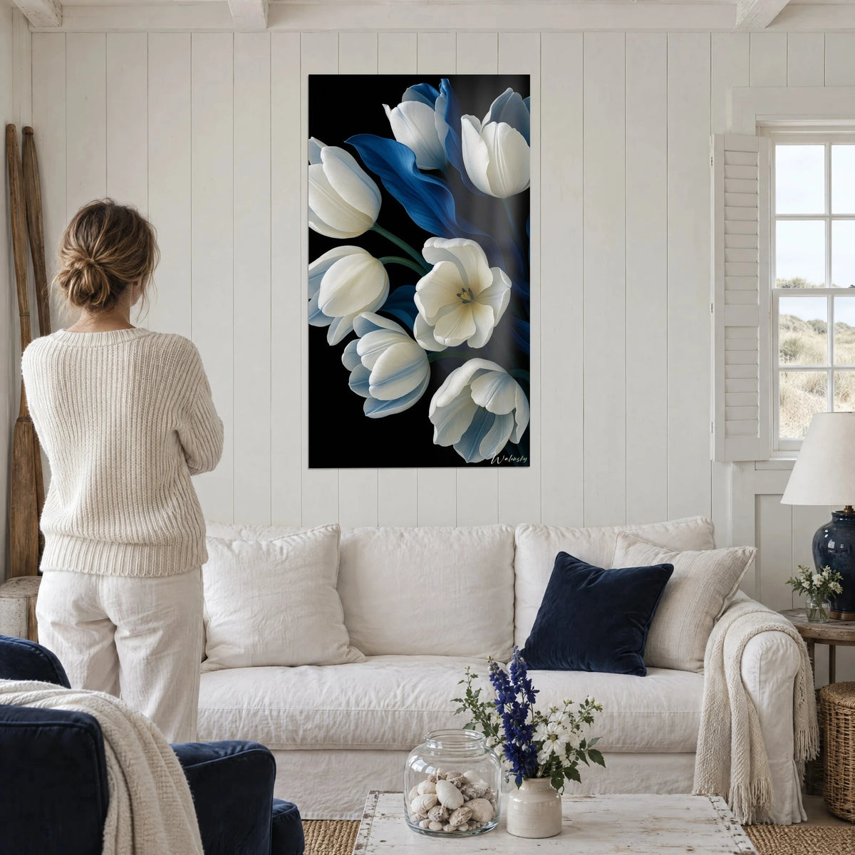 Tableau tulipes blanches et feuilles bleu cobalt sur fond noir, personne de dos, au-dessus d'un canapé dans un salon lumineux