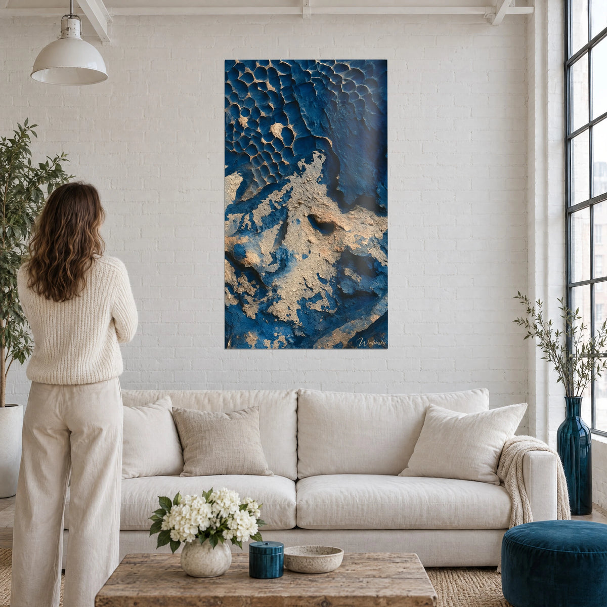 Tableau relief minéral bleu nuit et sable doré, alvéoles en nid d'abeille, femme de dos au-dessus d'un canapé dans un salon lumineux