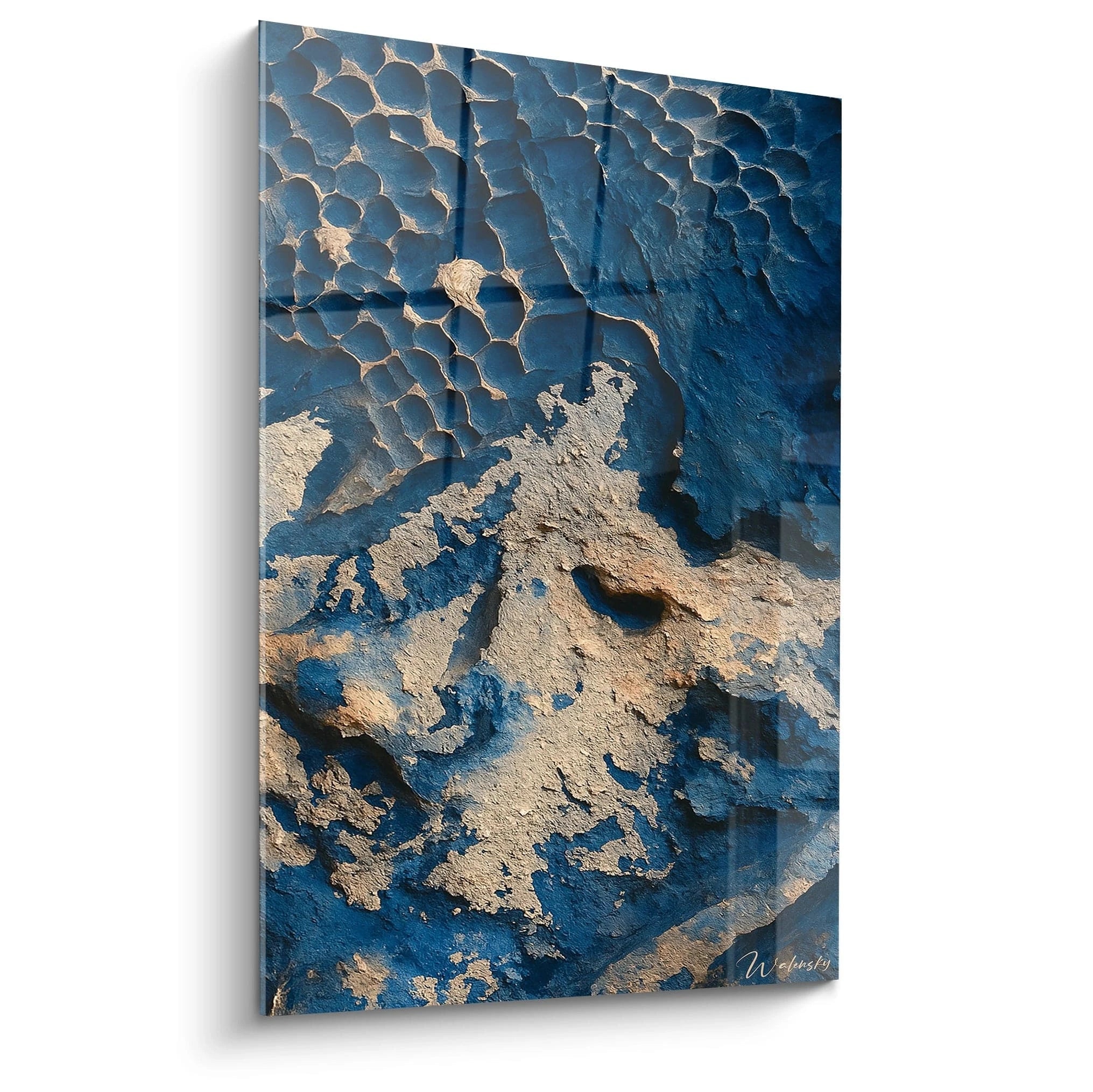 Un tableau vue aérienne représentant des formations géologiques alvéolaires, avec des structures cellulaires bleues profondes et des surfaces beiges érodées. Les textures craquelées et rugueuses créent un relief saisissant évoquant un paysage désertique vu du ciel.
