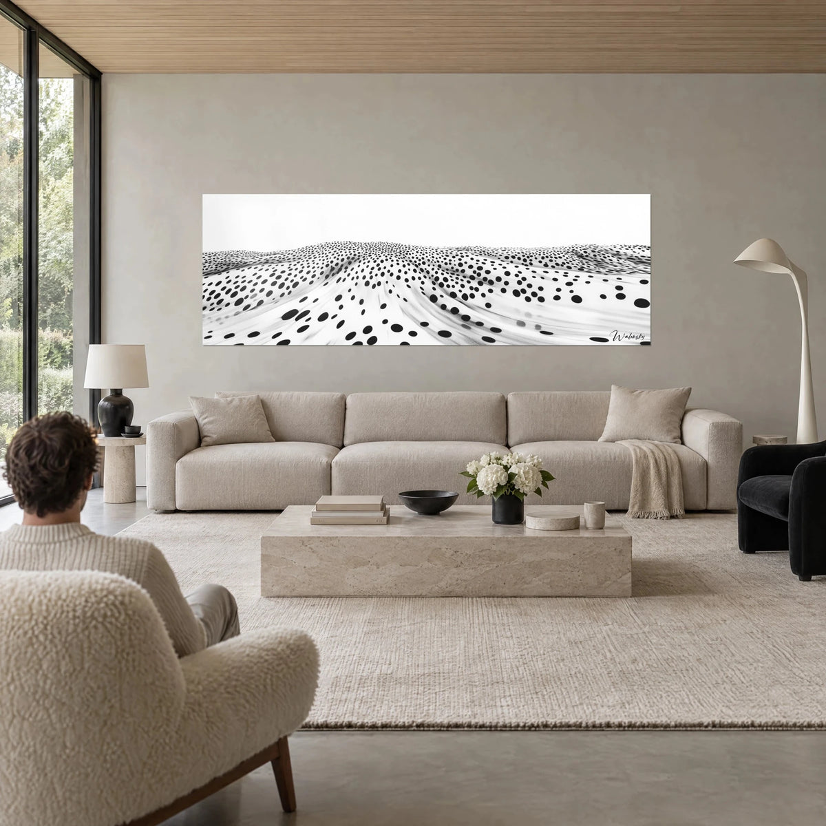 Cuadro dunas punteadas en blanco y negro, olas de puntos sobre fondo claro, una persona de espaldas, encima de un sofá en un salón luminoso