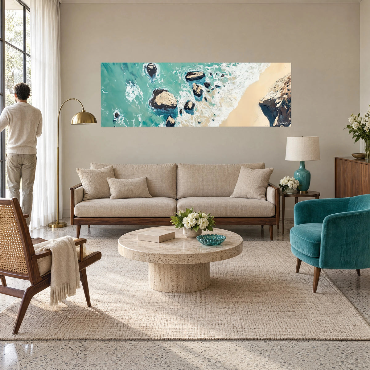 Schilderij luchtfoto van turquoise schuim over donkere rotsen en crèmekleurig zand, boven een bank in een lichte woonkamer