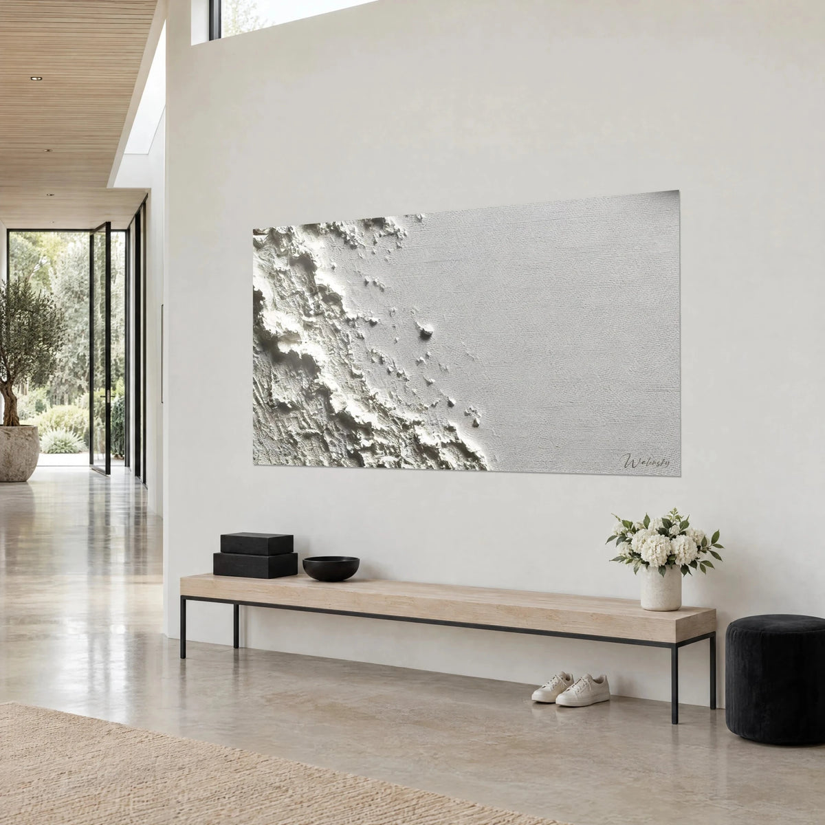 Tableau vague pétrifiée en reliefs ivoire sur fond gris clair, galet sombre, mur blanc, banc en bois, dans une maison d'architecte