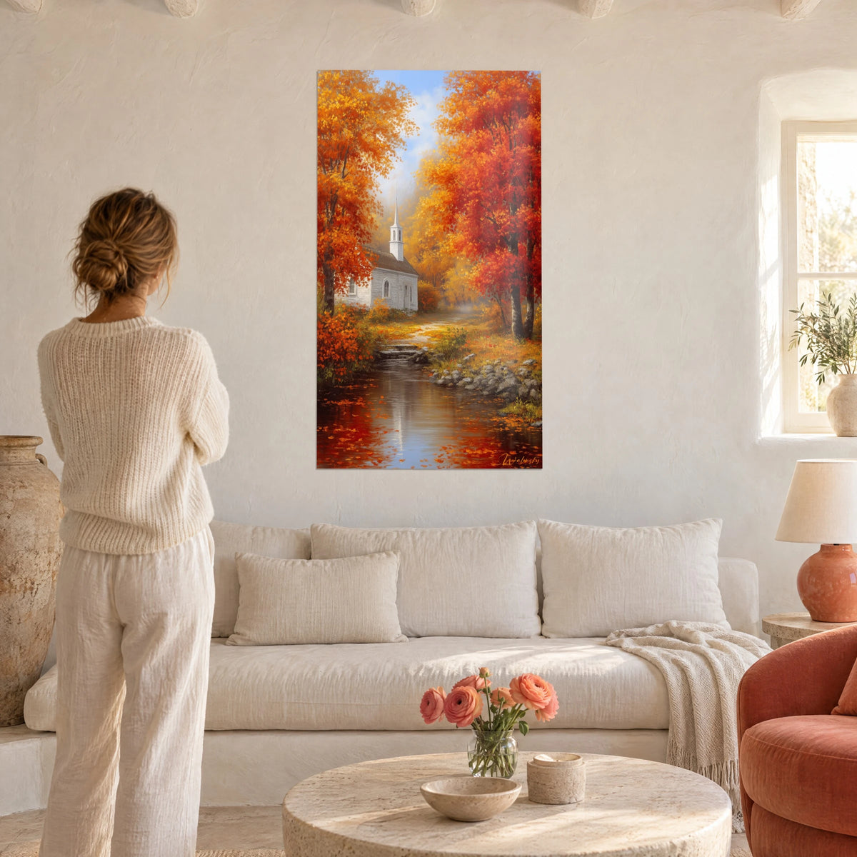 Tableau petite chapelle blanche dans les érables orange et or, femme de dos, au-dessus d'un canapé dans un salon lumineux