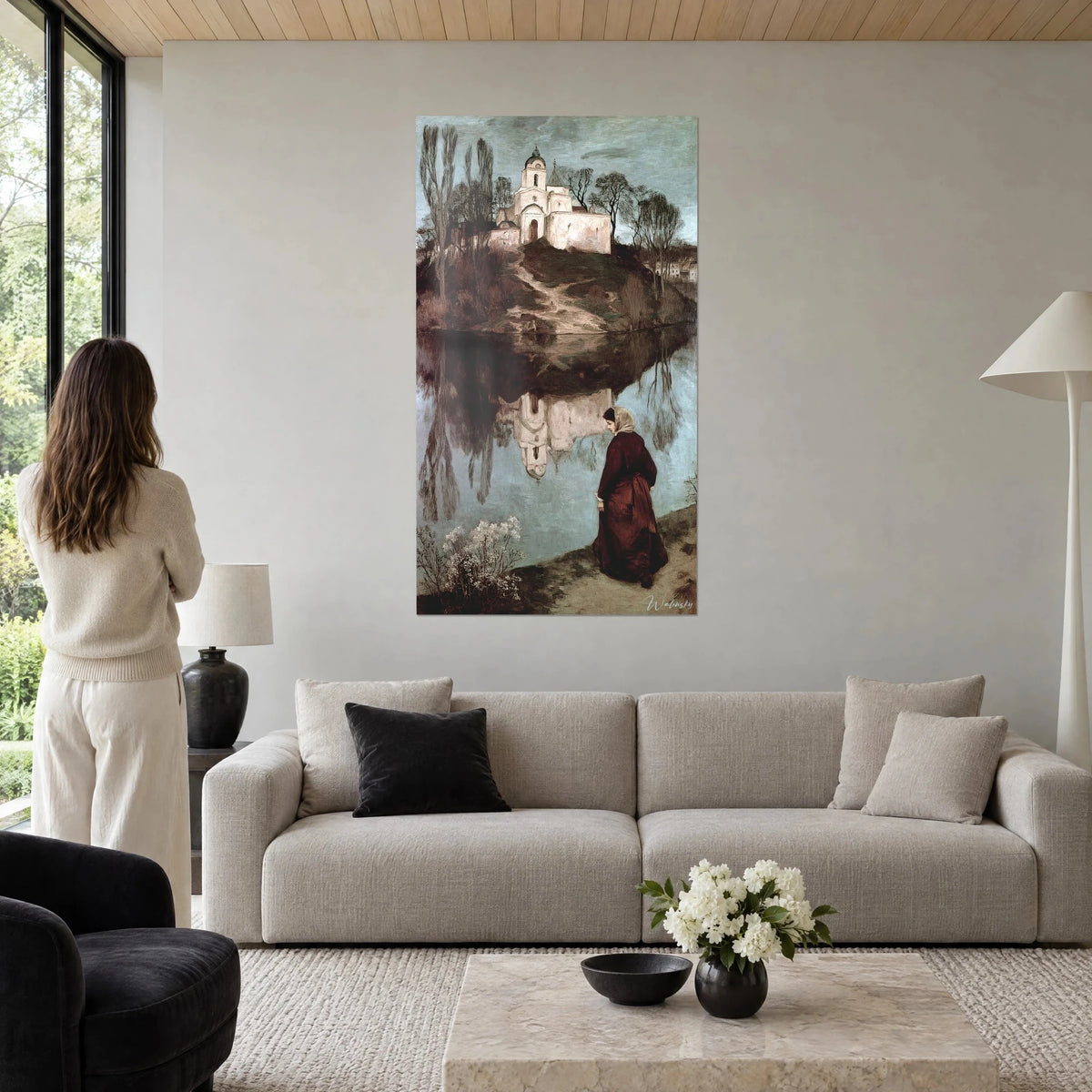 Gemälde einer weißen Kapelle auf ihrem Hügel, Frau im bordeauxroten Kleid, graublaues Wasser, über einem Sofa in einem hellen Wohnzimmer