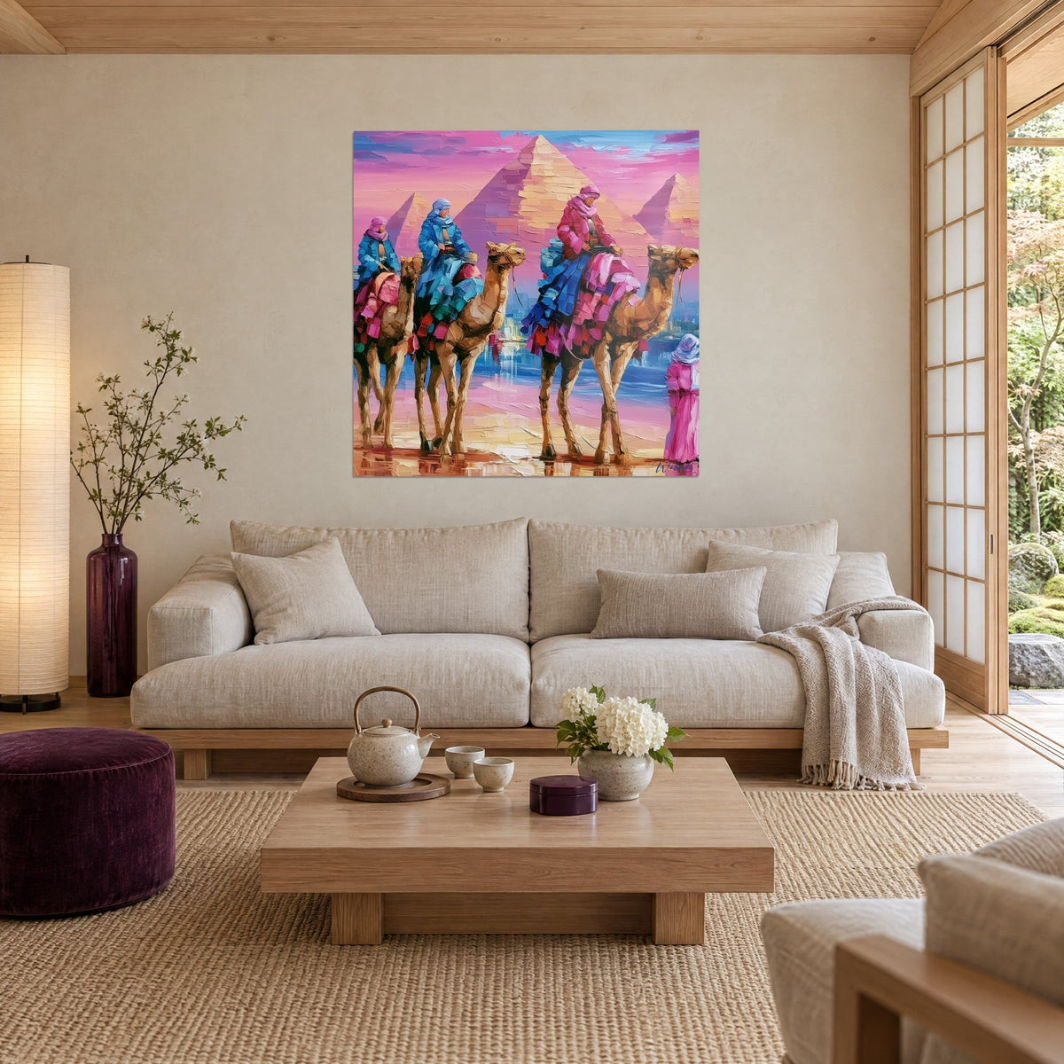 Gemälde Kamelkarawane in ockerfarbenen Tönen vor rosa Pyramiden, türkisfarbene und fuchsiafarbene Reiter, über einem Sofa in einem hellen Wohnzimmer