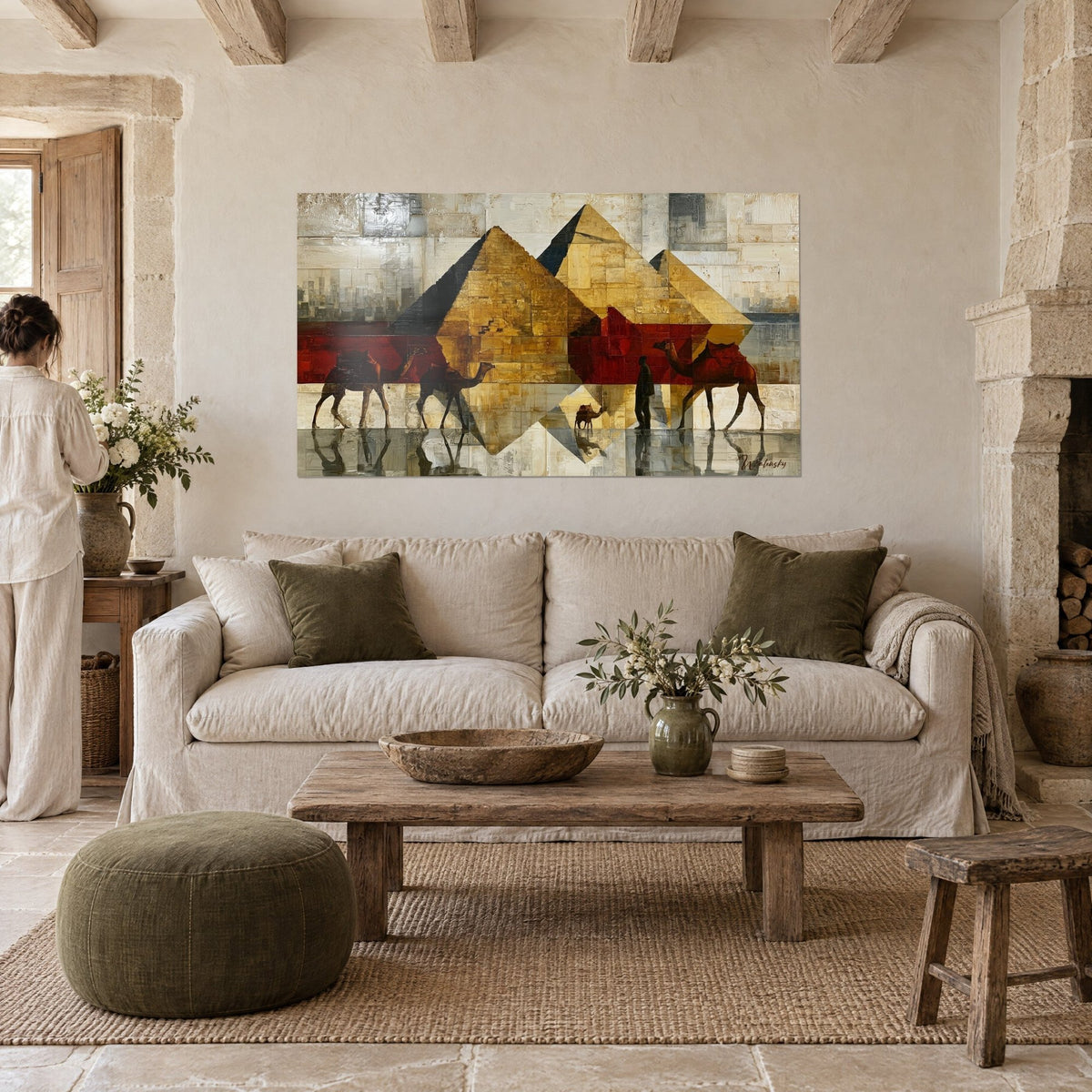 Tableau trois pyramides ocre doré, chameaux rouge brique et reflets miroités, une personne de dos, au-dessus d'un canapé dans un salon lumineux