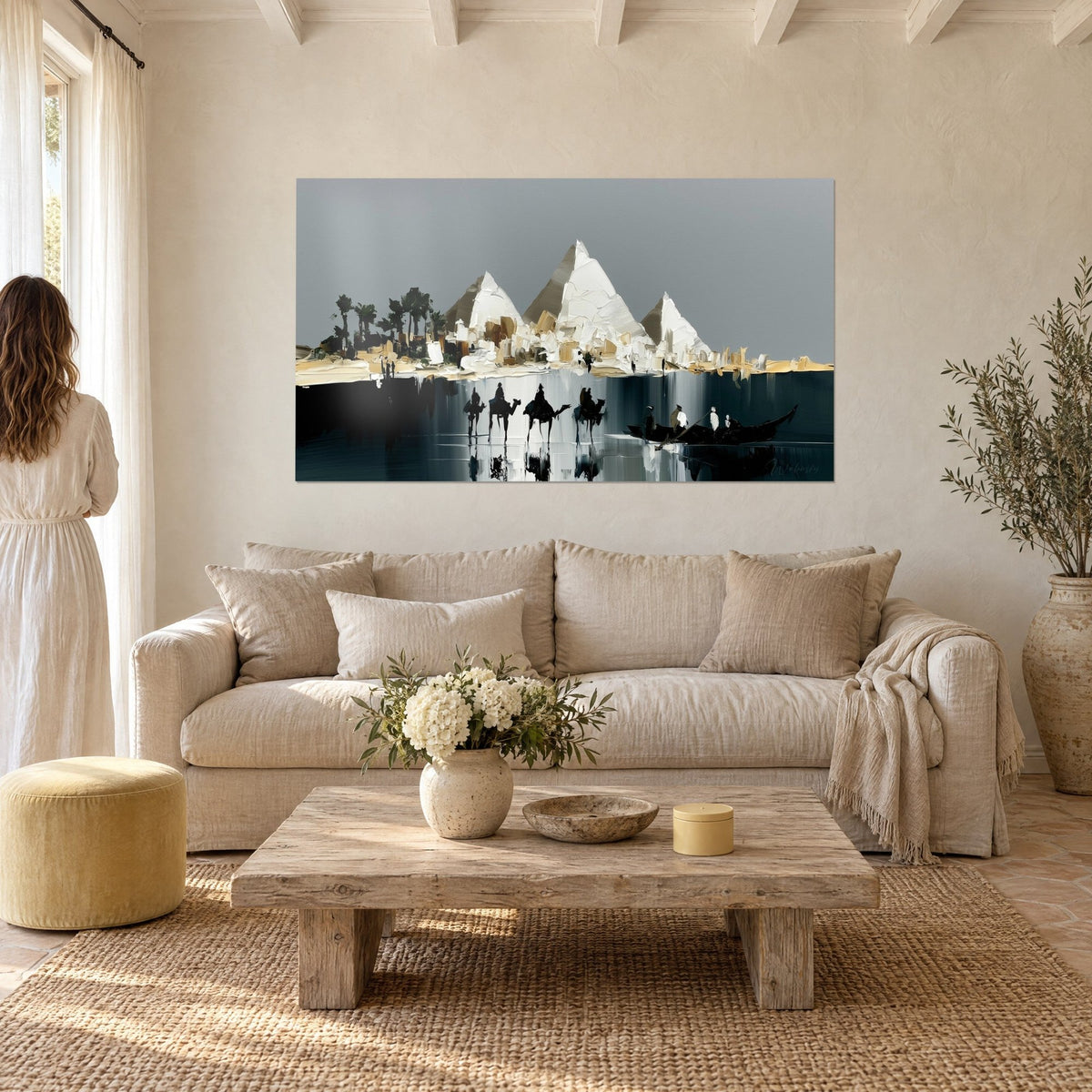 Gemälde mit drei dick aufgetragenen weißen Pyramiden und schwarzen Kamelen über dunklem Wasser, grauer Himmel, über einem Sofa in einem hellen Wohnzimmer