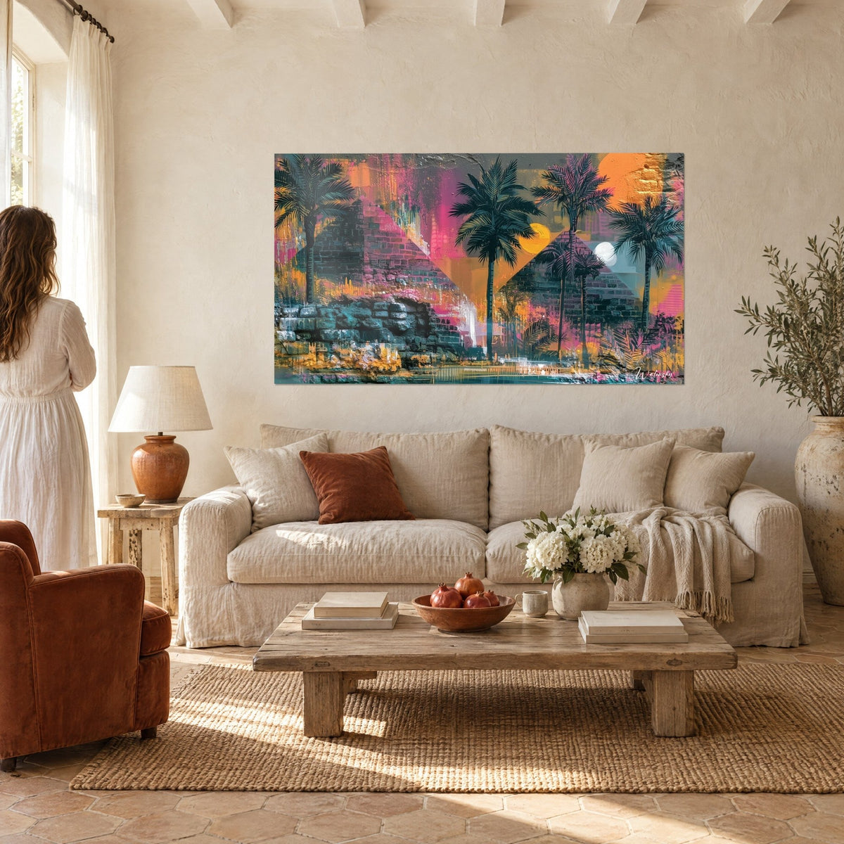 Wall art black palm trees in front of orange and pink pyramids, two moons golden and white, above a sofa in a bright living room