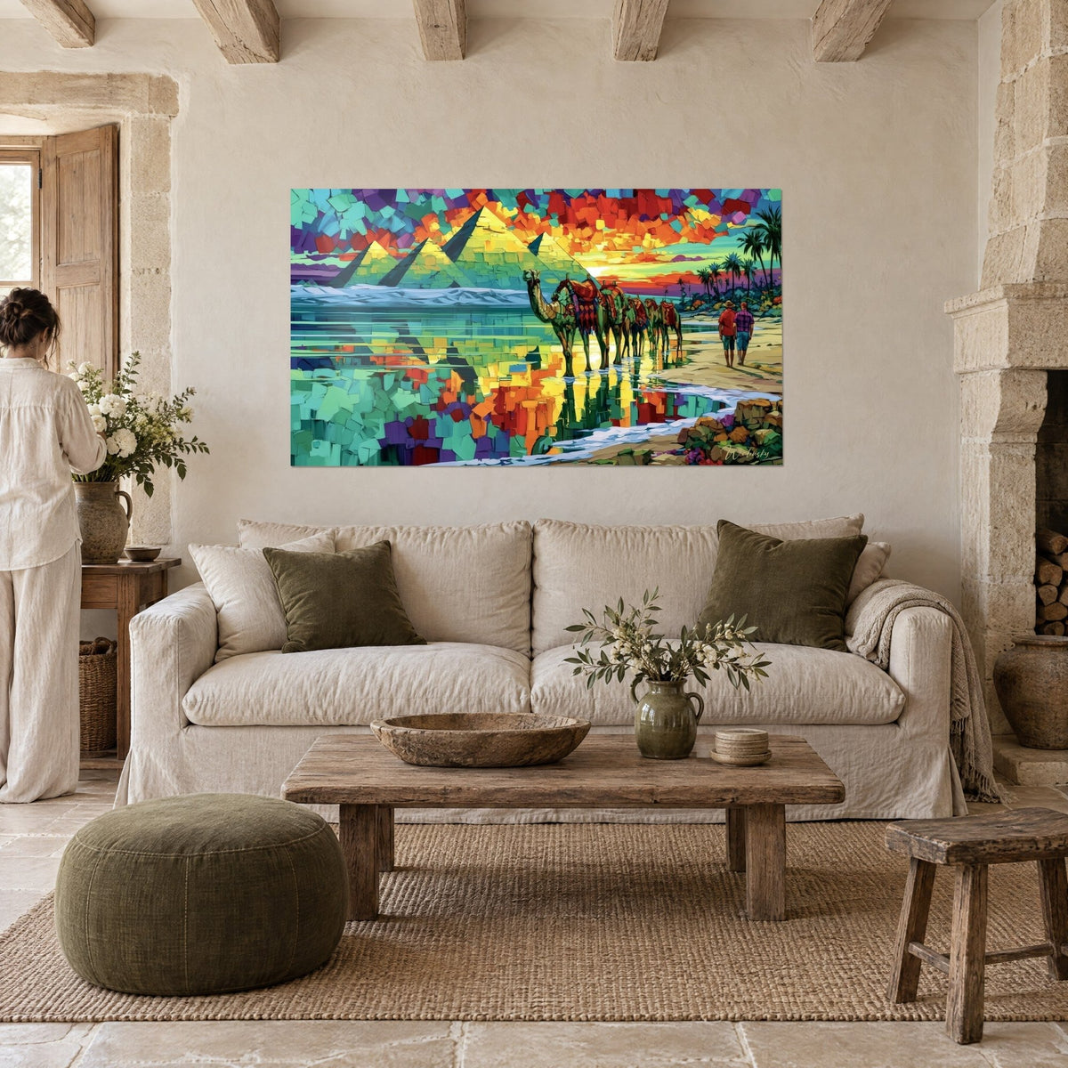 Gemälde türkisfarbene Pyramiden mit grünen Flanken unter einem rotorangefarbenen Himmel, eine Frau von hinten, über einem Sofa in einem hellen Wohnzimmer