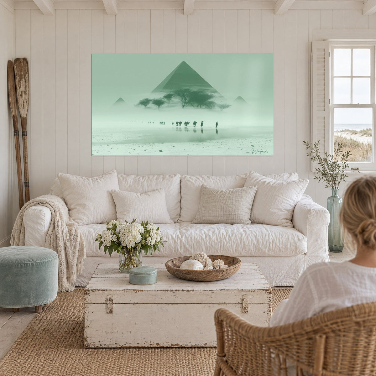 Wall art with a misty pale green pyramid and acacia trees in silhouette, reflections on the water, sage green and white, above a sofa in a bright living room