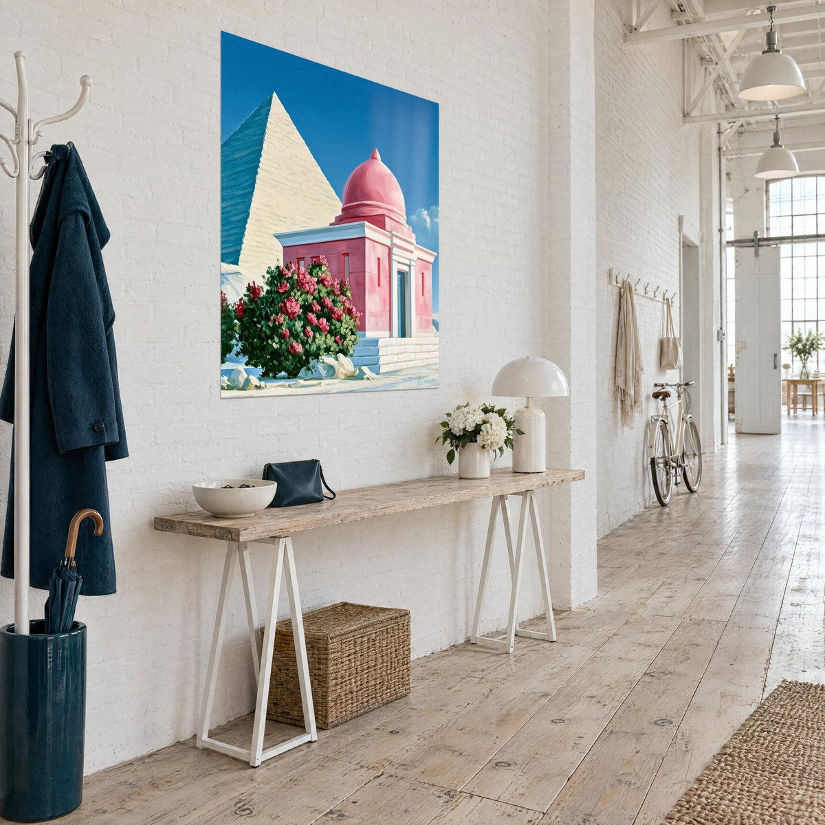 Wall art golden pyramid rising behind a small pink temple, fuchsia roses and ultramarine sky, three-quarter view in a light hallway