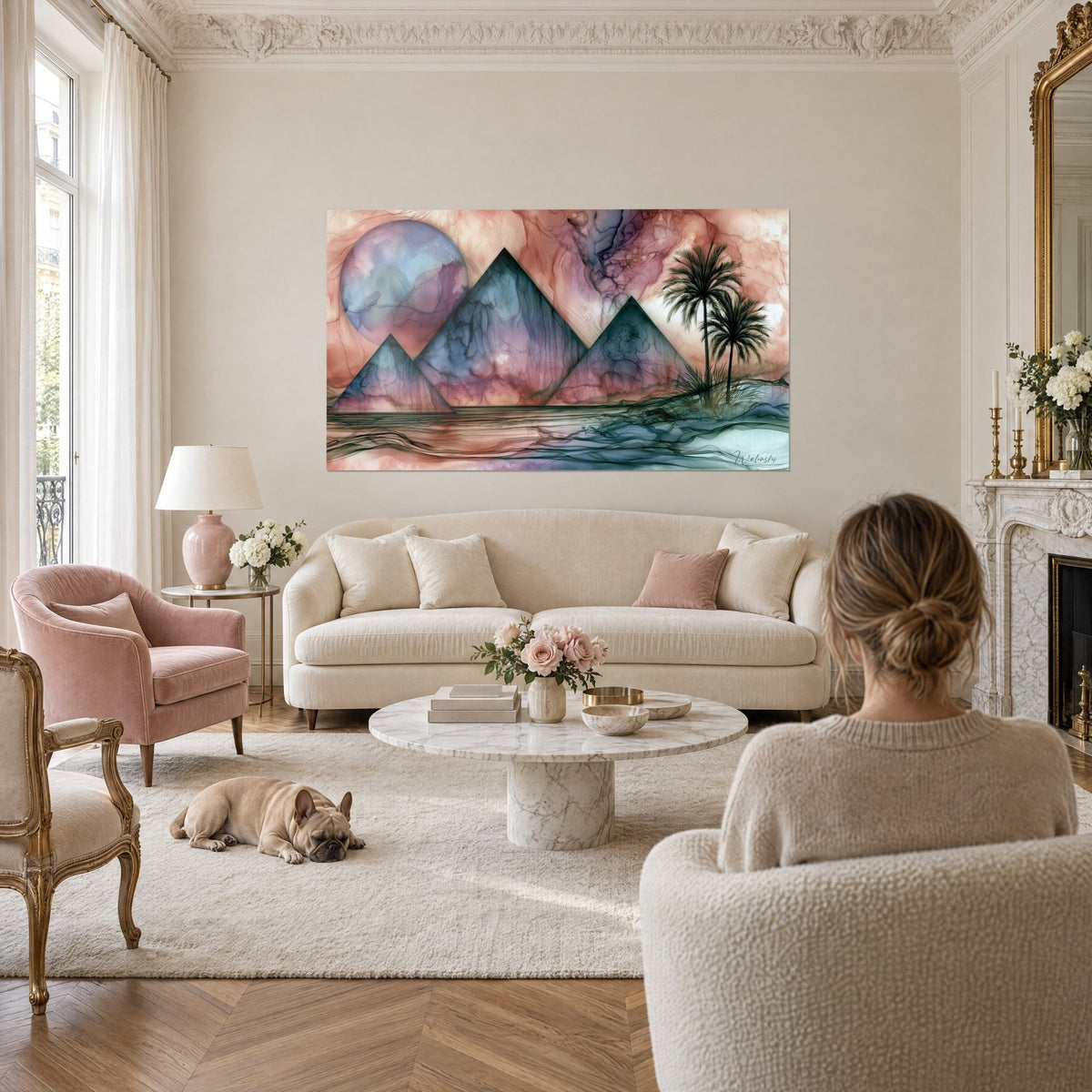 Gemälde drei Pyramiden in Nachtblau und Puderrosa unter einem lila Mond, eine Frau von hinten und ein Bulldogge über einem Sofa in einem hellen Wohnzimmer