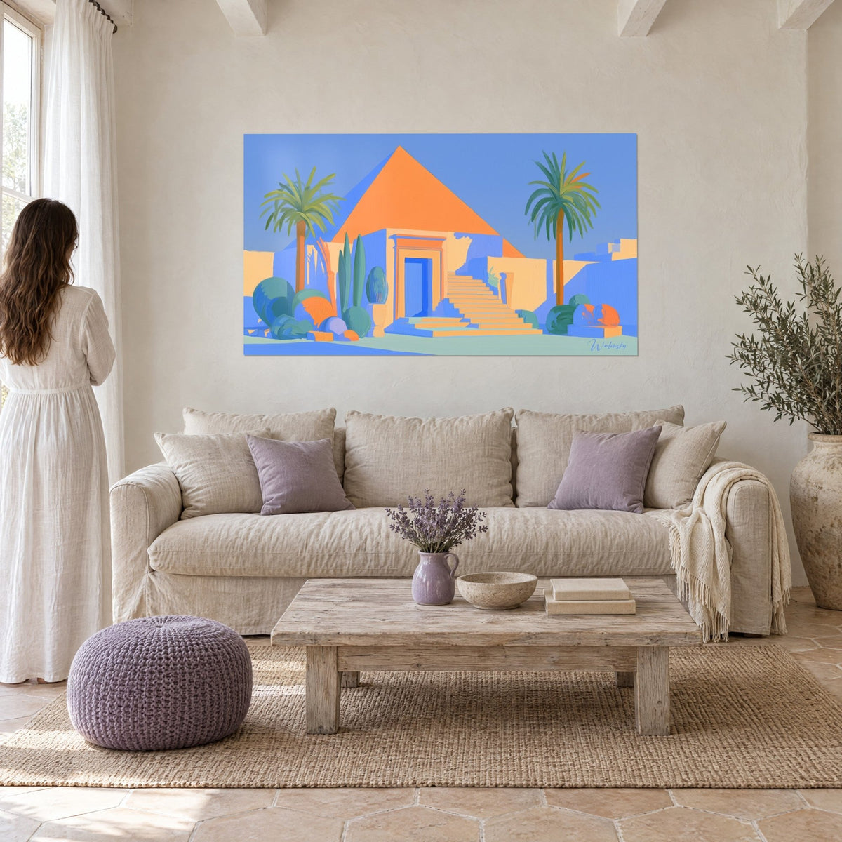 Wall art vivid orange pyramid under a blue sky, two palm trees and a stone staircase, woman seen from behind above a sofa in a bright living room