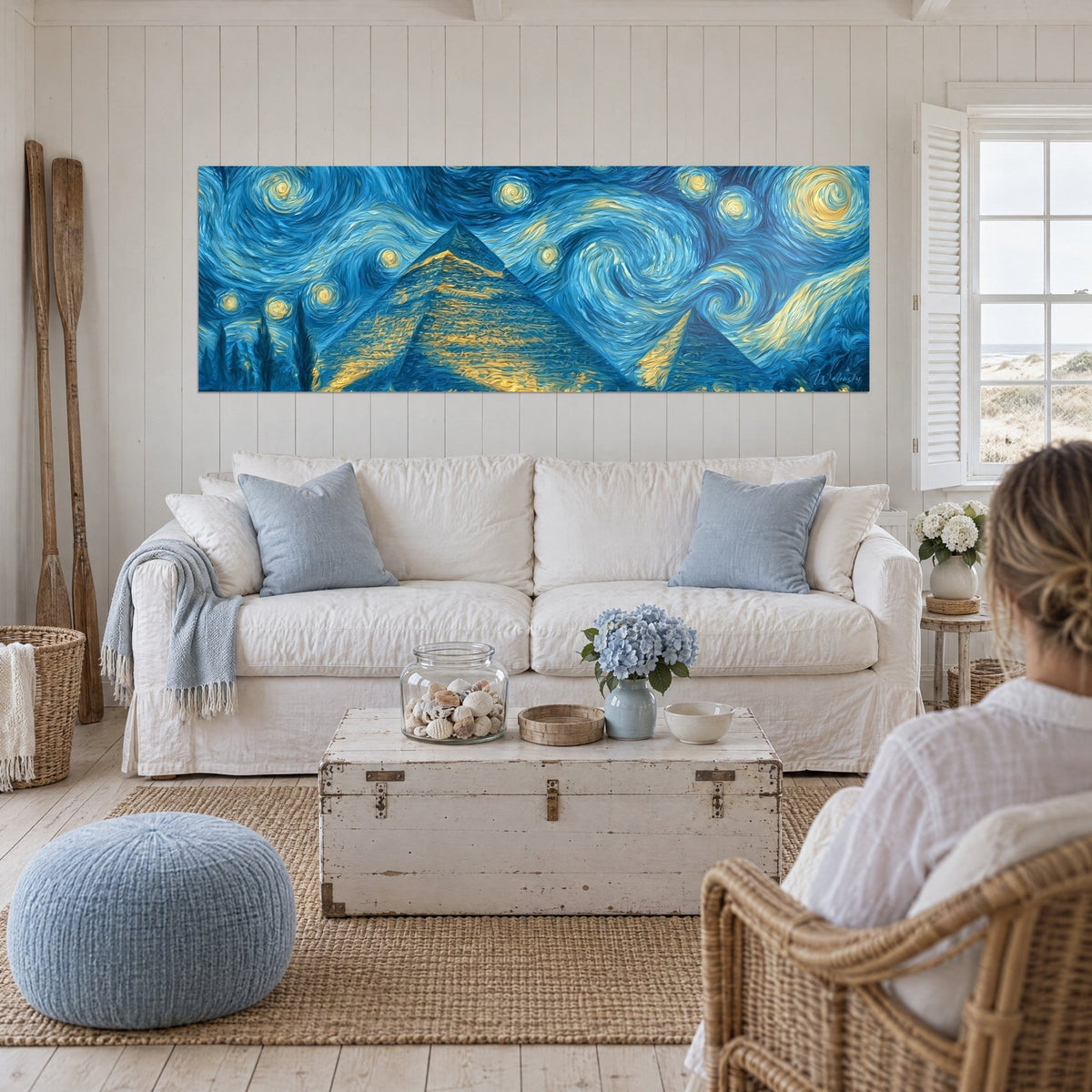 Wall art golden pyramids under a swirling blue sky, two people seen from behind, above a sofa in a bright living room