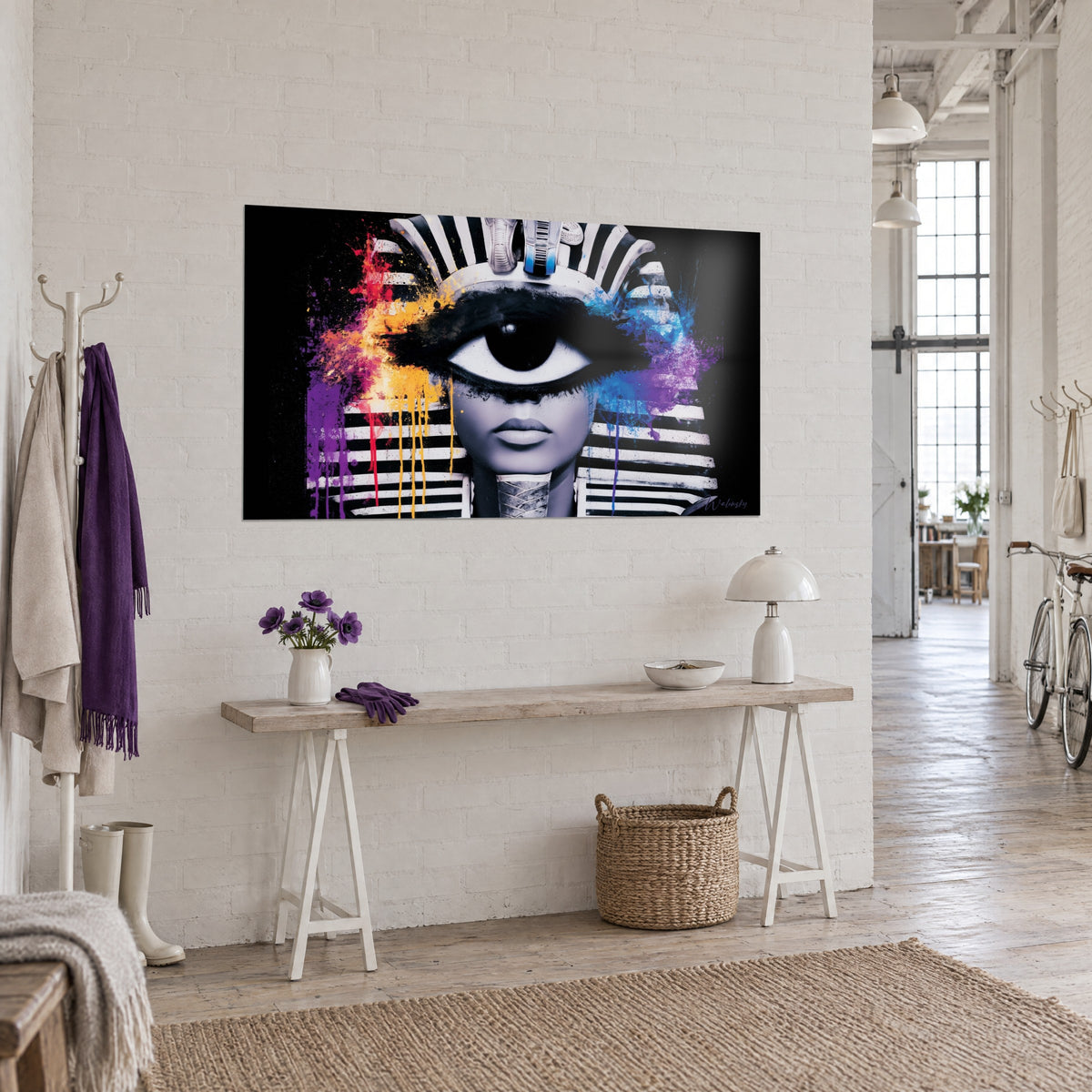 Cuadro máscara egipcia de mirada hipnótica, labios grises, goteos amarillos y azul cobalto, en una pared blanca junto a una consola de madera