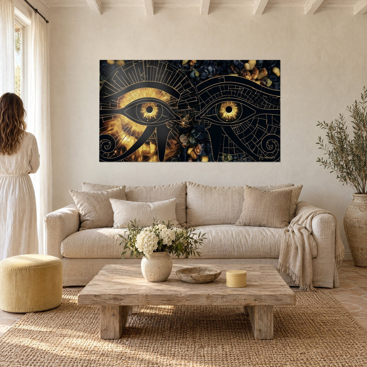Cuadro Ojos de Horus perfilados en negro, iris ámbar radiantes sobre guijarros oscuros, una mujer de espaldas, encima de un sofá en un salón luminoso