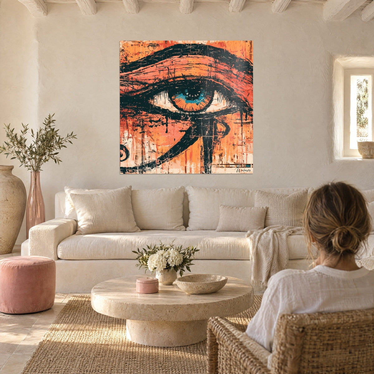 Wall art Eye of Horus painted in orange and black, turquoise blue iris, woman seen from behind, above a sofa in a bright living room