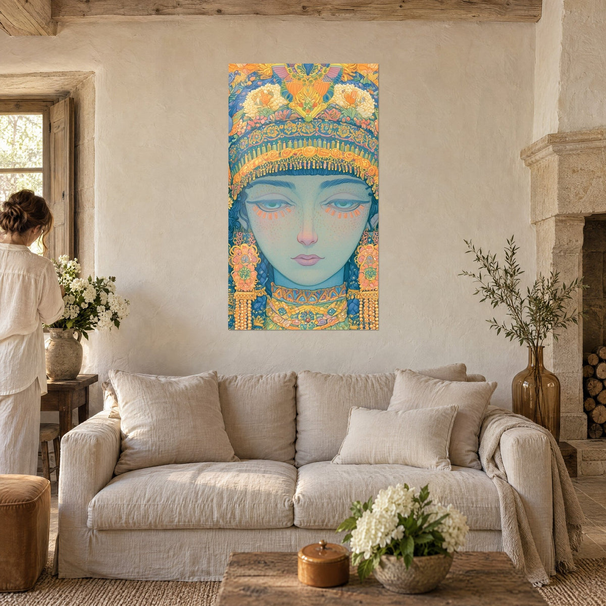Cuadro de rostro egipcio de ojos aguamarina bajo un tocado floral dorado, en azul y naranja, dos personas de espaldas sobre un sofá en un salón luminoso
