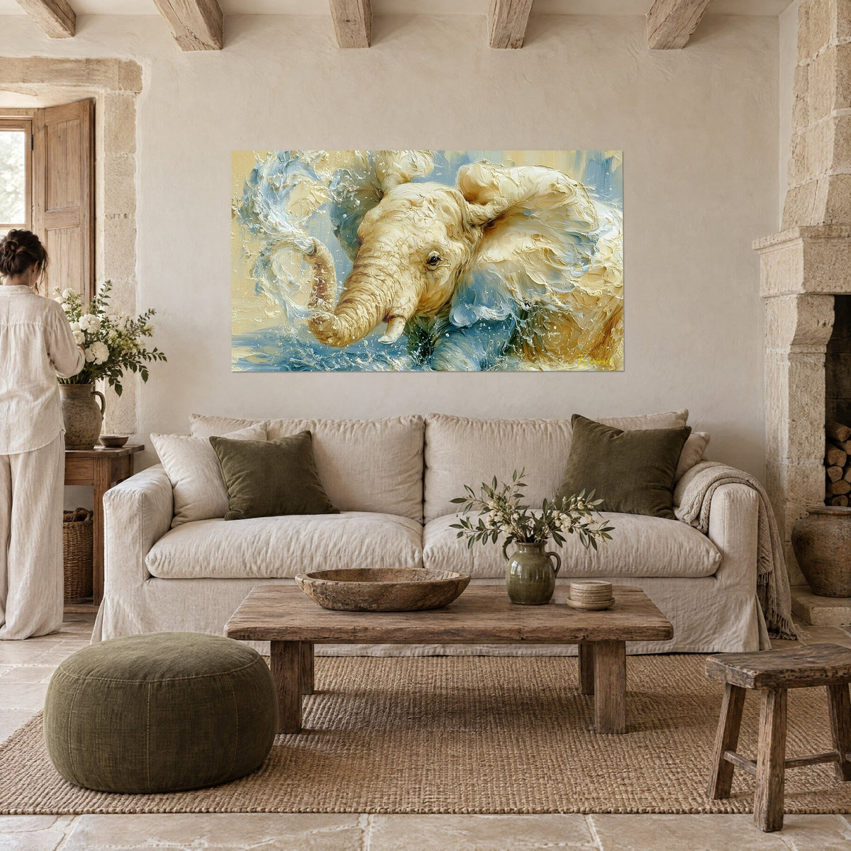 Cuadro cría de elefante color crema salpicando agua, trompa levantada, azul cielo y ocre, persona de espaldas, sobre un sofá en un salón luminoso