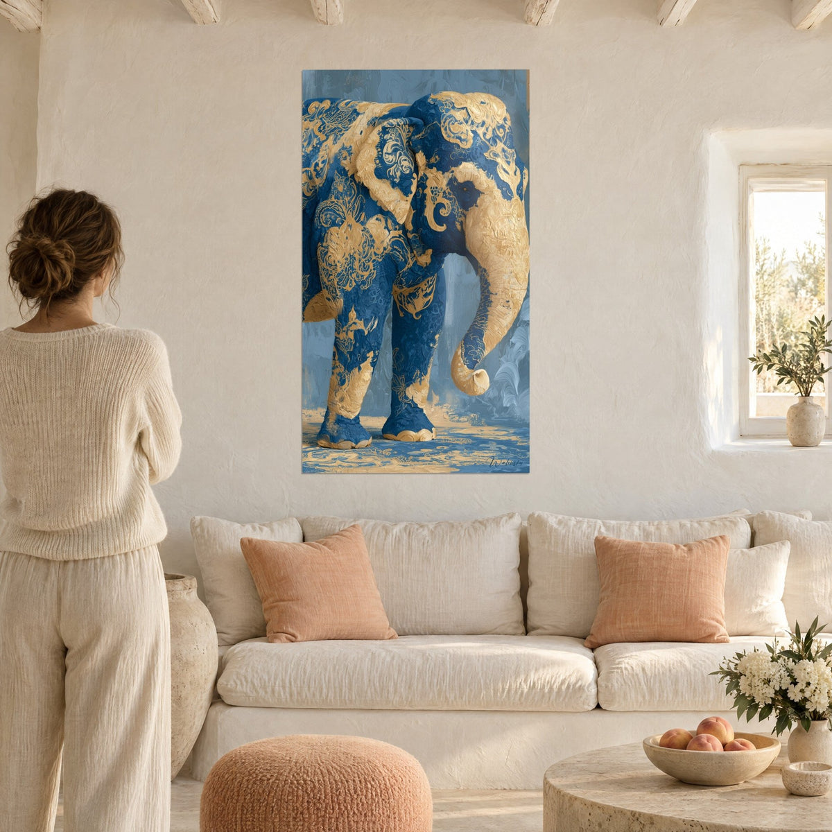 Gemälde Elefant in Marineblau mit goldenen barocken Schnörkeln, betrachtet von einer Frau von hinten, über einem Sofa in einem hellen Wohnzimmer