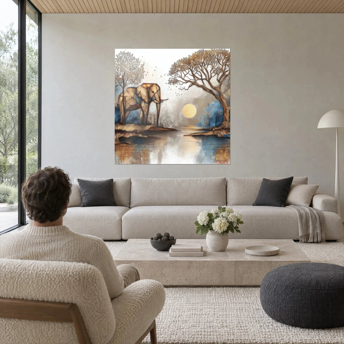 Wall art elephant with golden facets in front of a pale sun, slate blue sky, a person seen from behind, above a sofa in a bright living room
