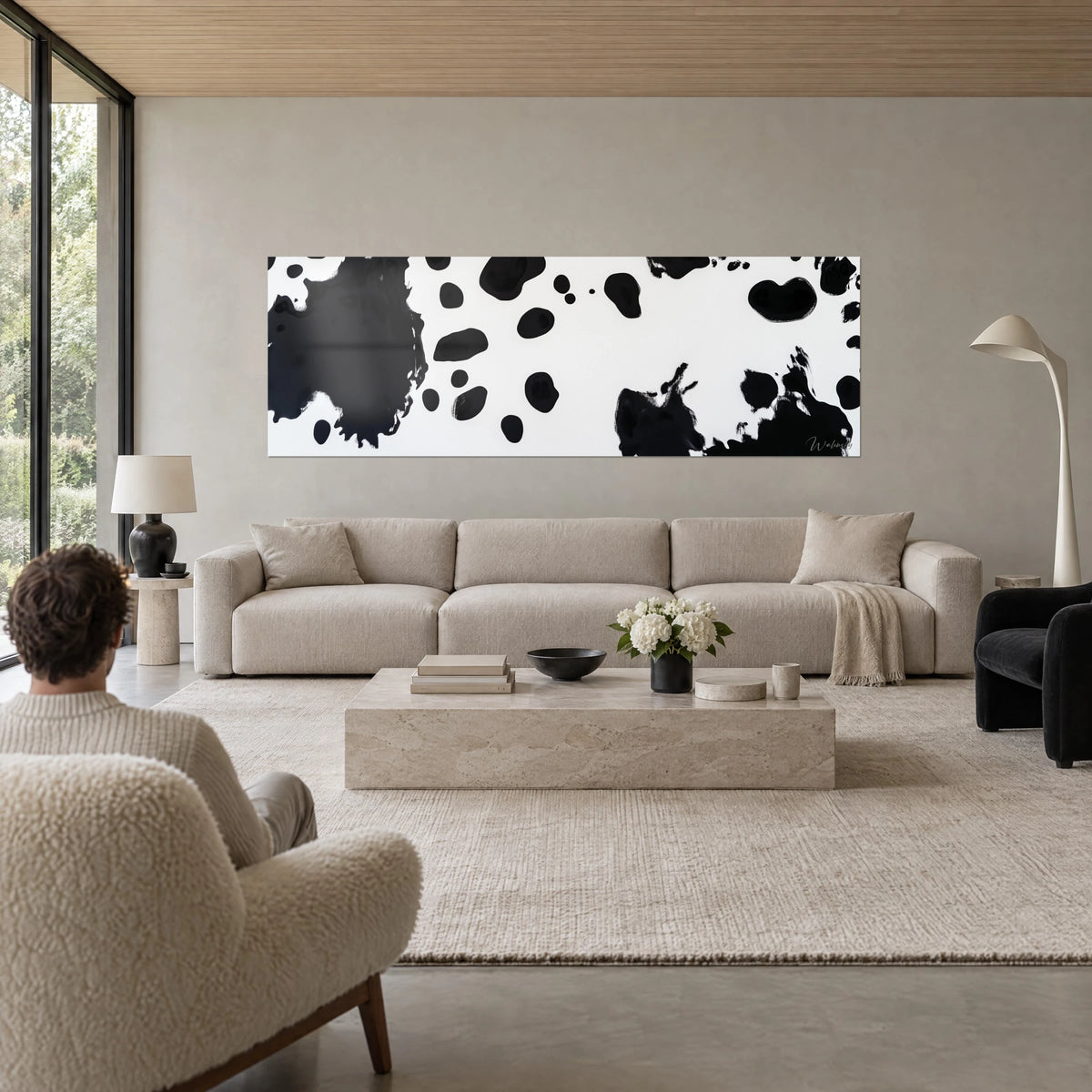 Schilderij met zwarte inktvlekken op witte achtergrond, grote plas links, spatten rechts, boven een bank in een lichte woonkamer