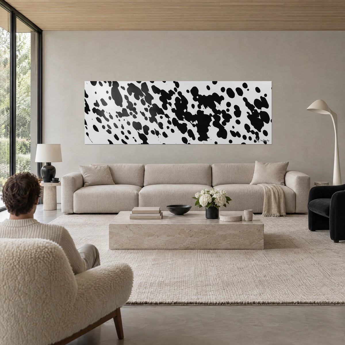 Cuadro con salpicaduras de tinta negra sobre fondo blanco crema, formato panorámico, encima de un sofá en un salón luminoso