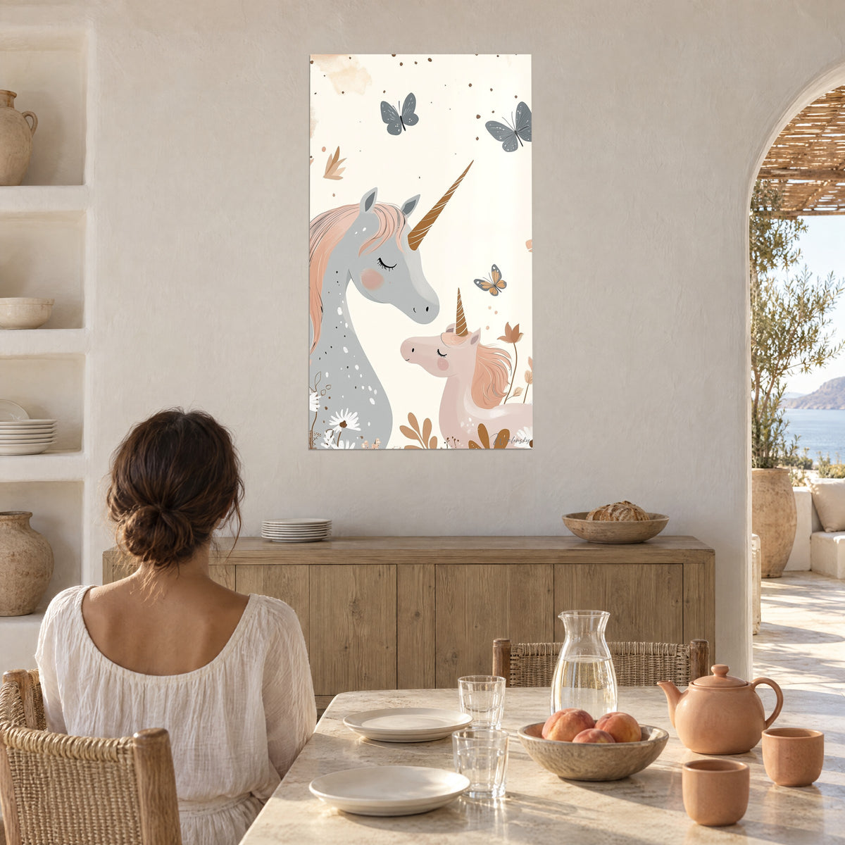 Cuadro pareja de unicornios de mejillas rosadas, cuerno dorado, mariposa naranja y flores terracota, vista por una mujer a la mesa junto a un arco