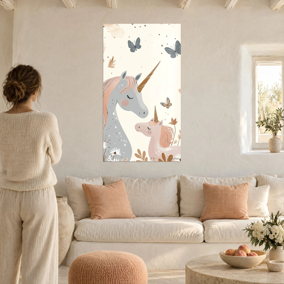 Tableau licorne grise au crin pêche et son poulain rose, papillons bleu-gris, face à une femme, au-dessus d'un canapé dans un salon lumineux