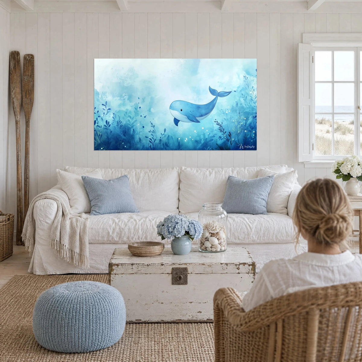 Gemälde eines verspielt lachenden Blauwals, der zwischen türkisfarbenen und indigoblauen Algen schwebt, eine Person von hinten, über einem Sofa in einem hellen Wohnzimmer