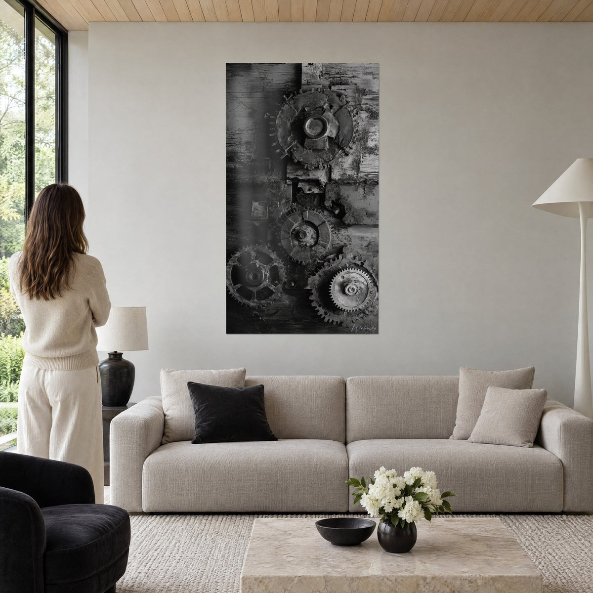Quadro ingranaggi arrugginiti in bianco e nero, ruote dentate grigie su legno patinato, donna di spalle, sopra un divano in un soggiorno luminoso