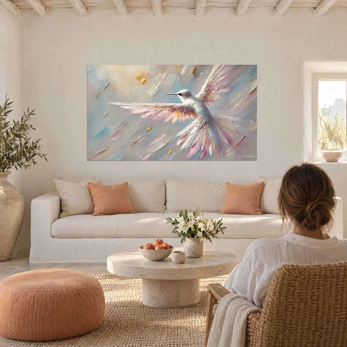 Wall art white hummingbird with wings spread, powder pink and gold feathers, pale blue background, above a sofa in a bright living room