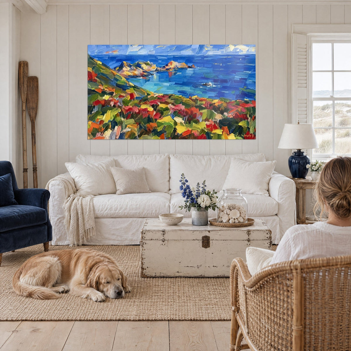 Gemälde Felsküste unter blauem Himmel, Pfad mit roten und grünen Blumen, türkisfarbenes Meer, über einem Sofa in einem hellen Wohnzimmer